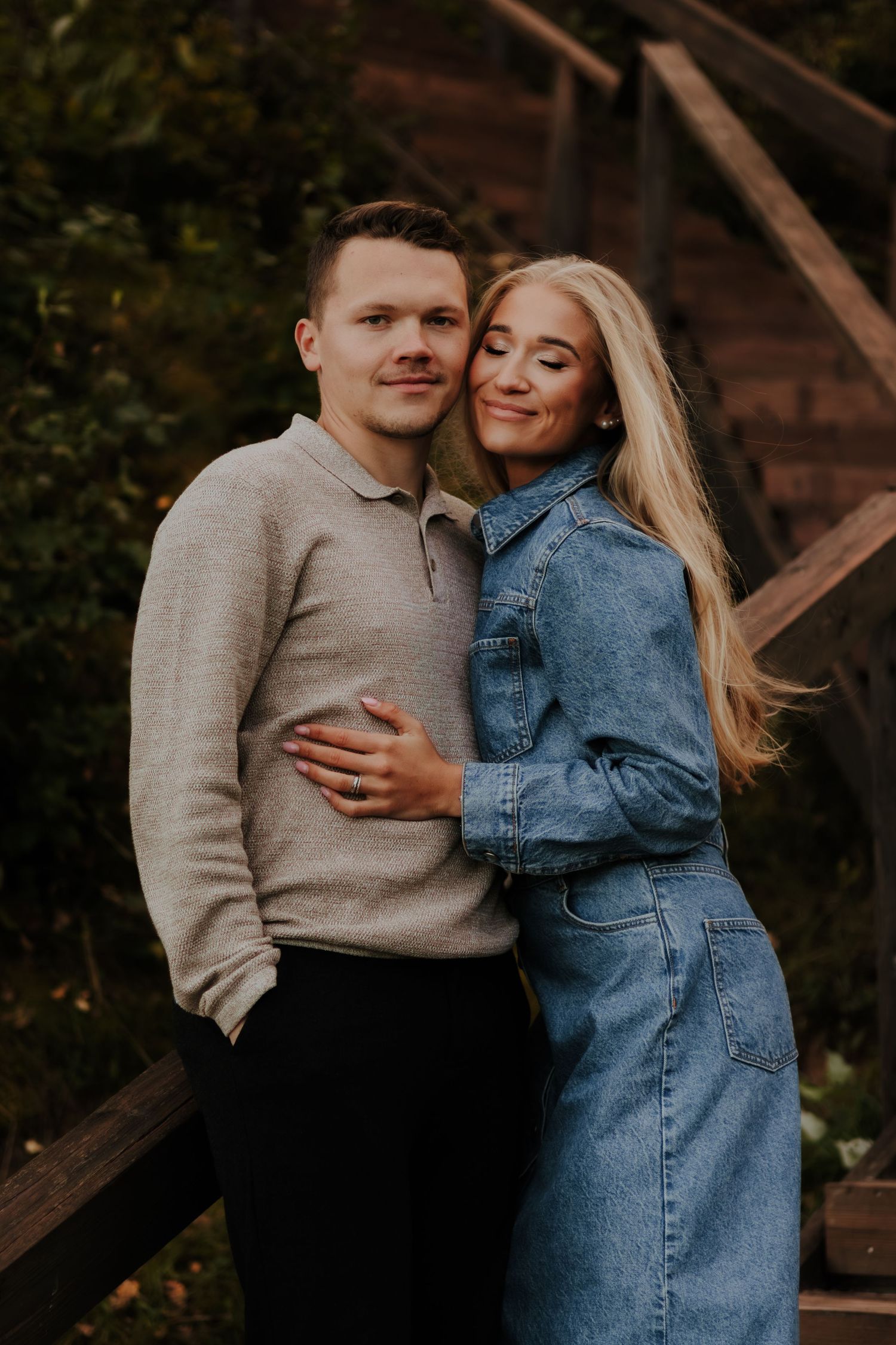 A couple embraces outdoors wearing a beige sweater and denim dress in a romantic autumn photoshoot.