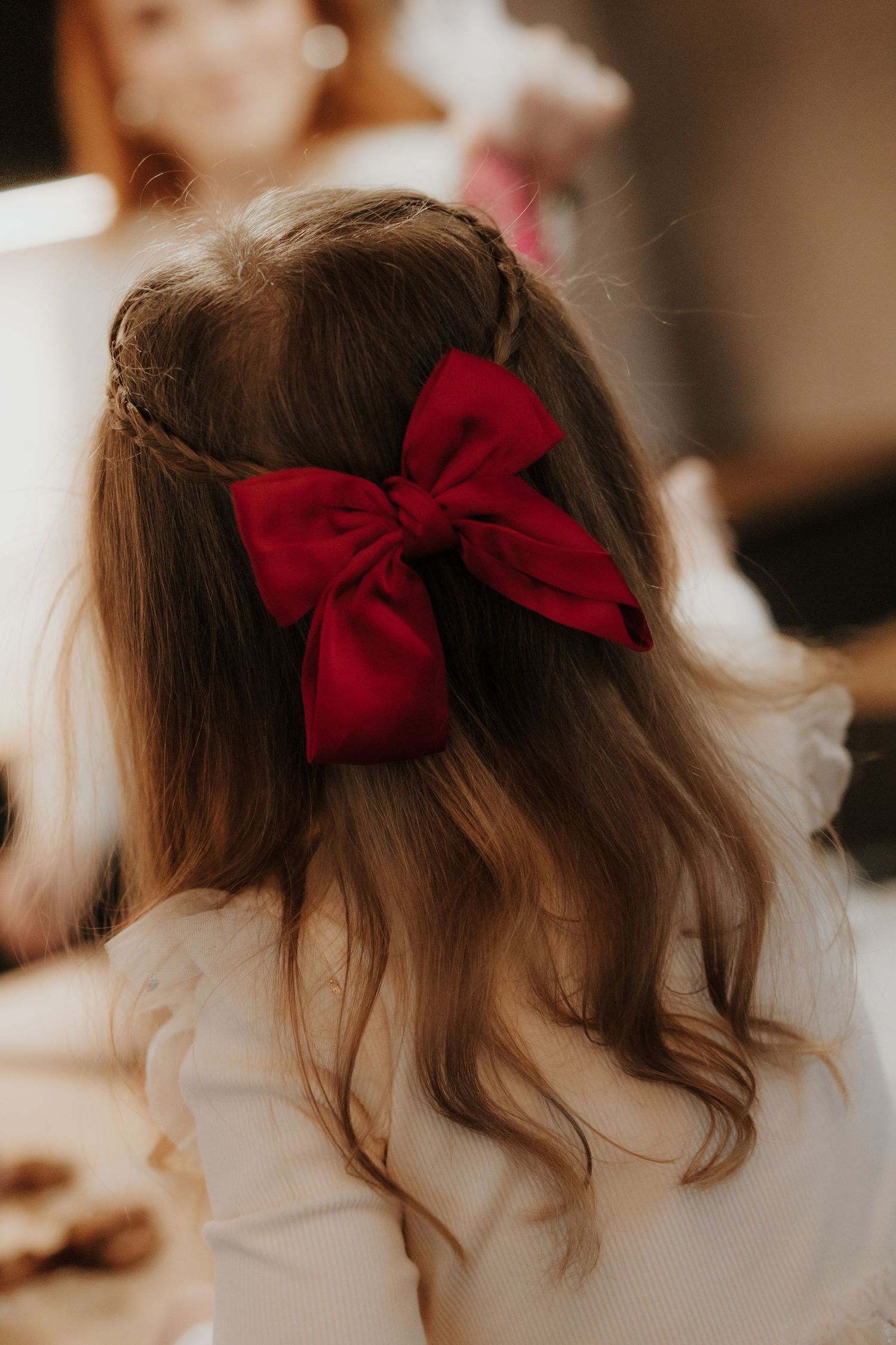 A large red velvet bow adorns brown wavy hair in a romantic hairstyle detail shot.