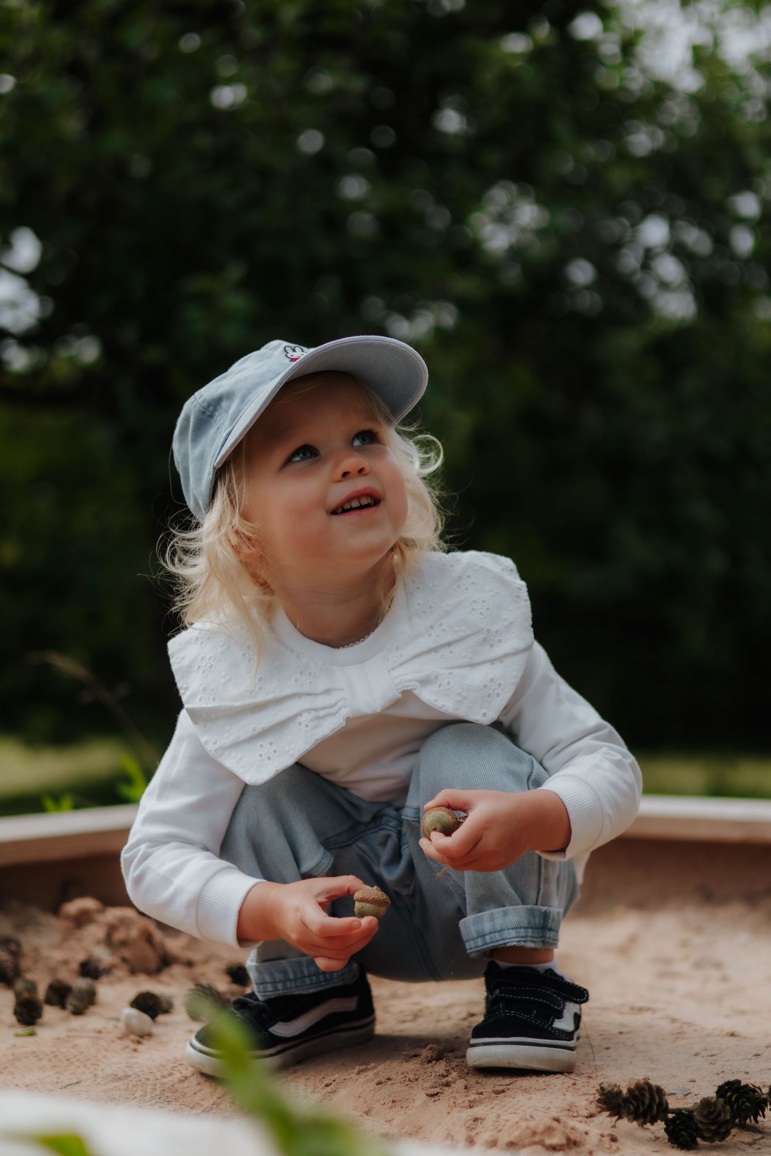 A child in white and gray clothing crawls and explores in a dirt or sand play area outdoors.