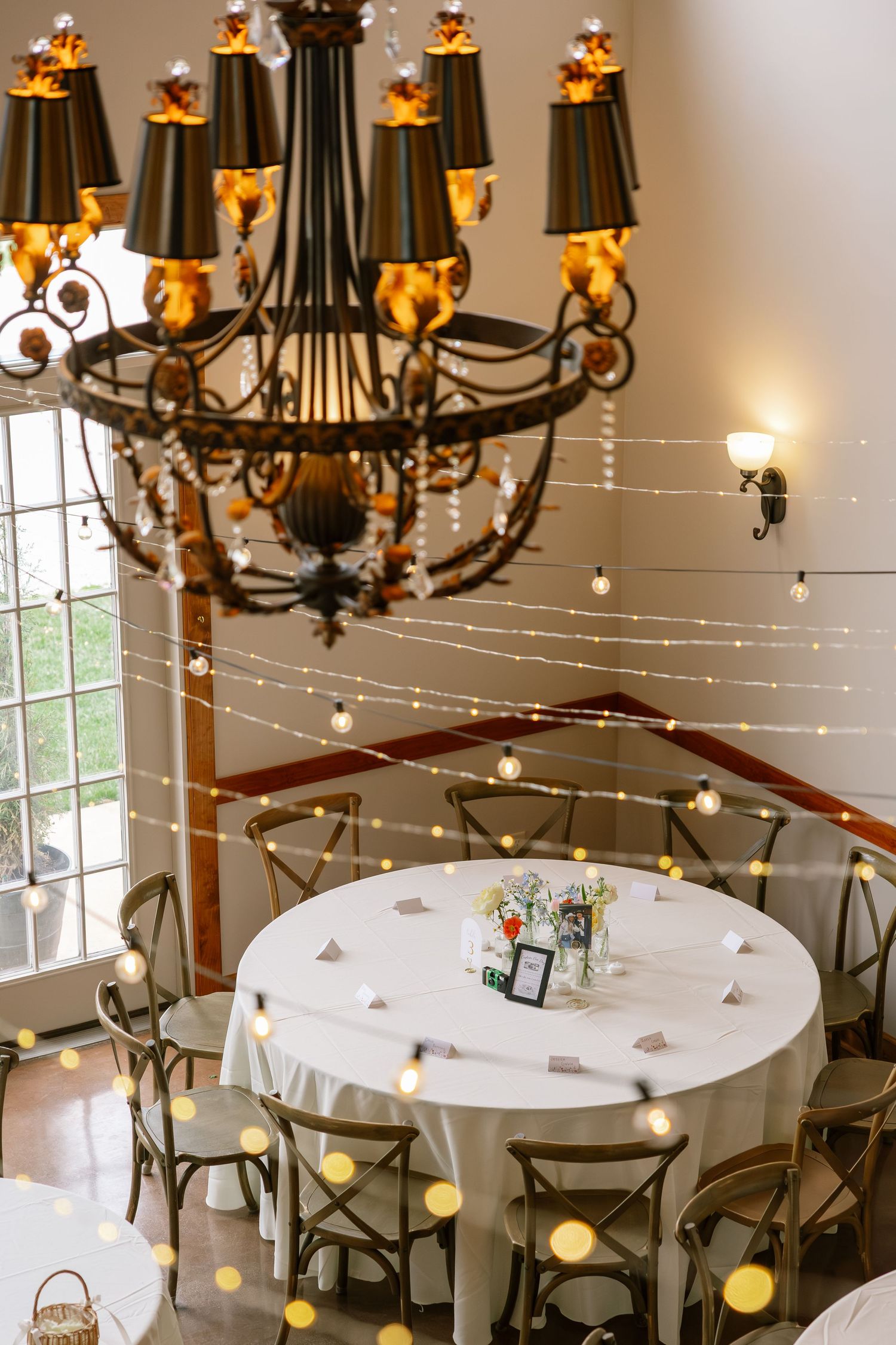 Elegant wedding reception venue with a wrought iron chandelier, string lights, and round tables with white linens.