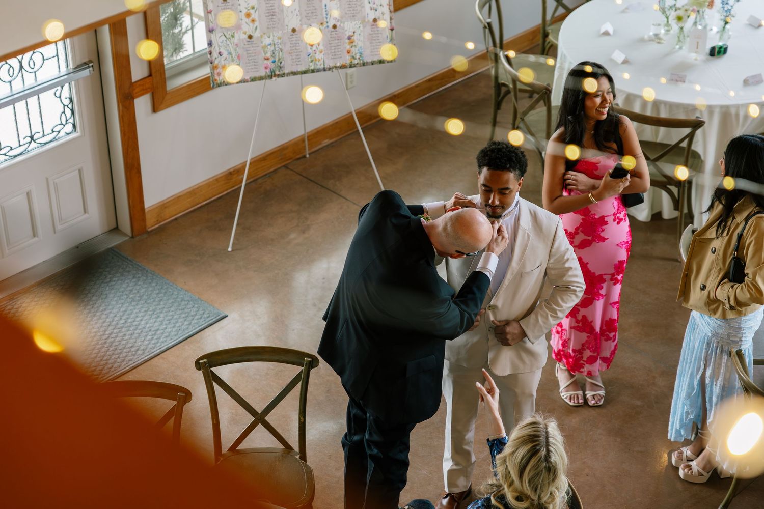 Overhead view of wedding guests greeting the newlyweds indoors with string lights and warm ambient lighting.