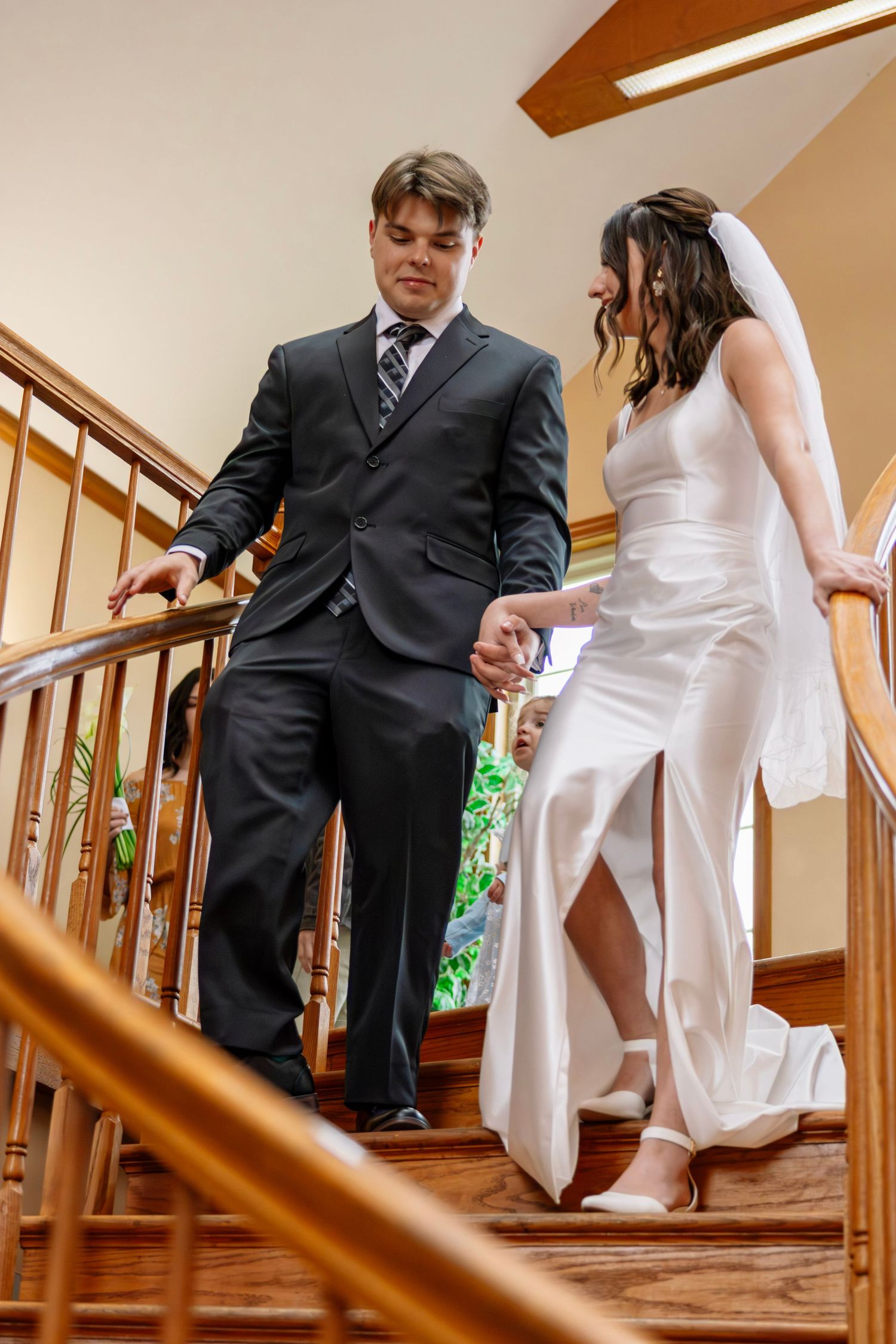 Newlywed couple walks hand in hand down wooden staircase following their indoor wedding ceremony.