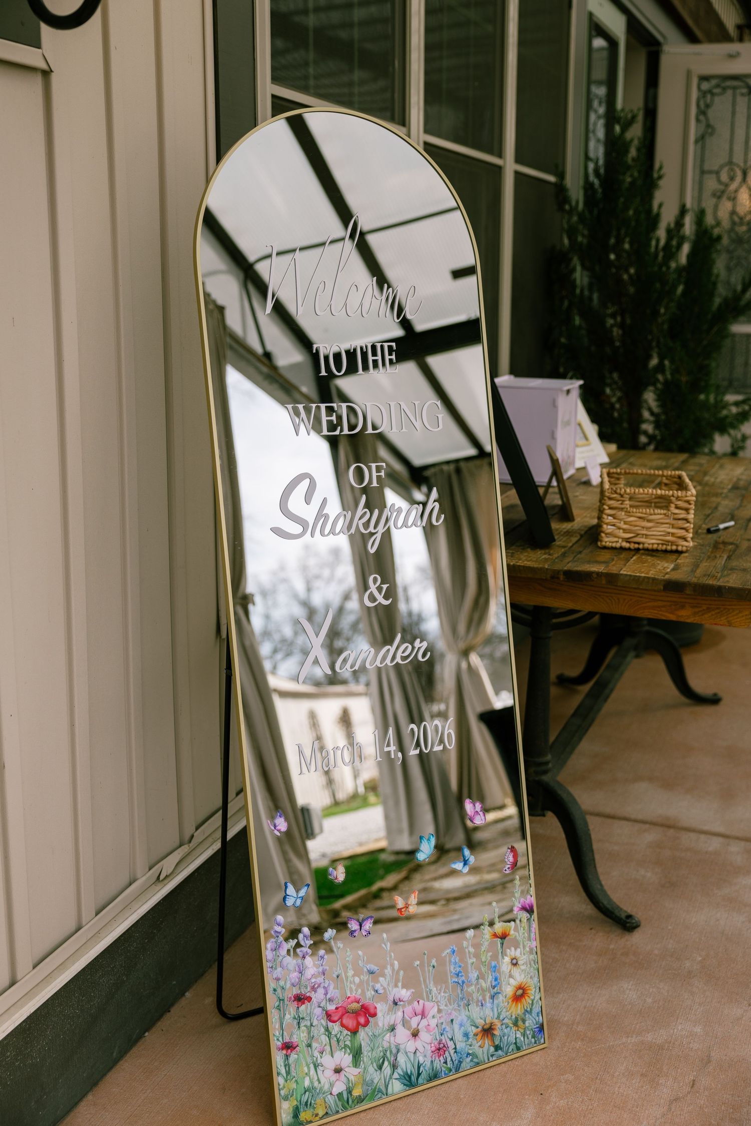 Gold arched mirror wedding welcome sign for Shakyah and Xander's wedding on March 14, 2026 with floral design.