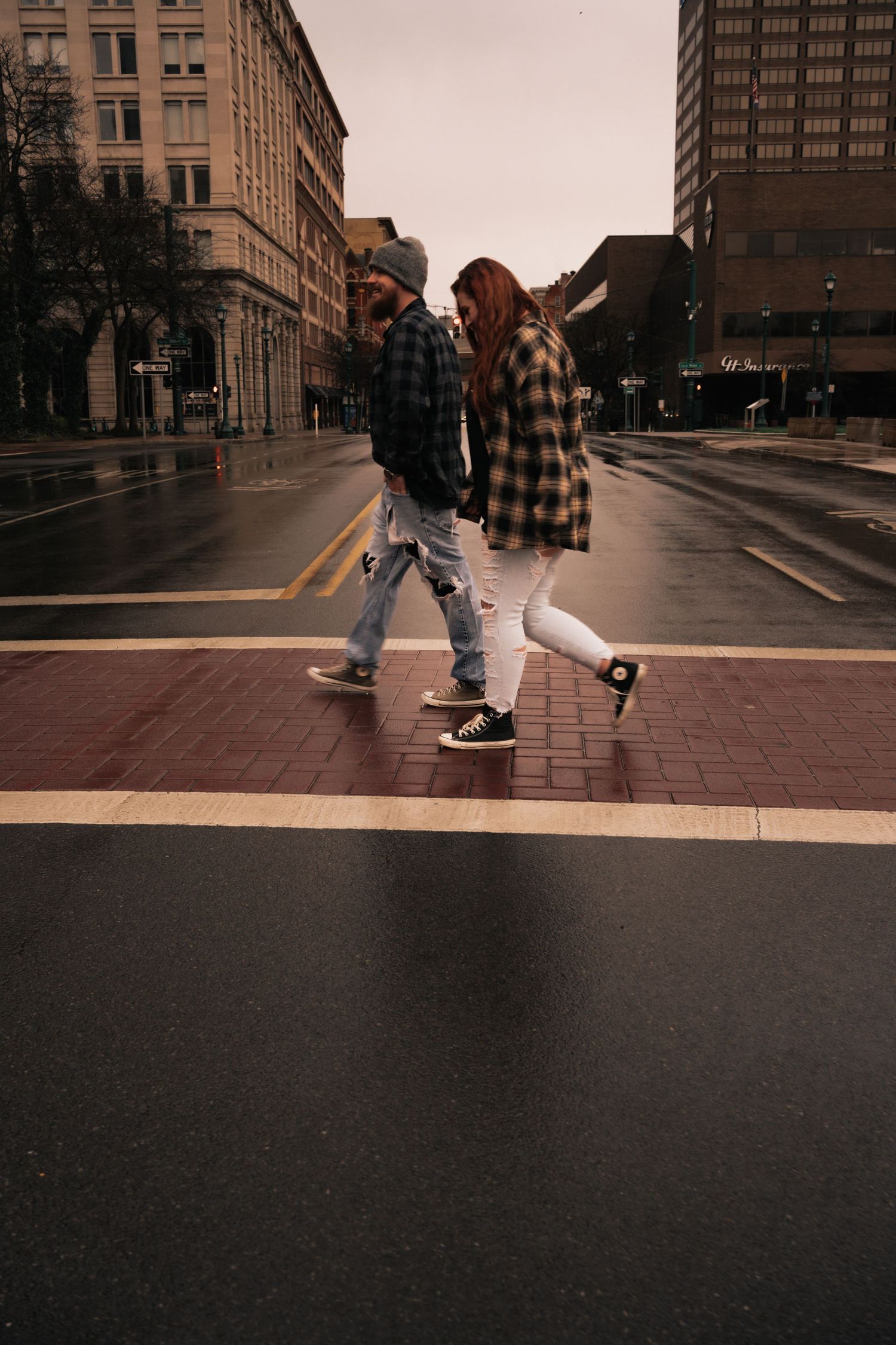 Couple crossing urban intersection on brick crosswalk on overcast day.