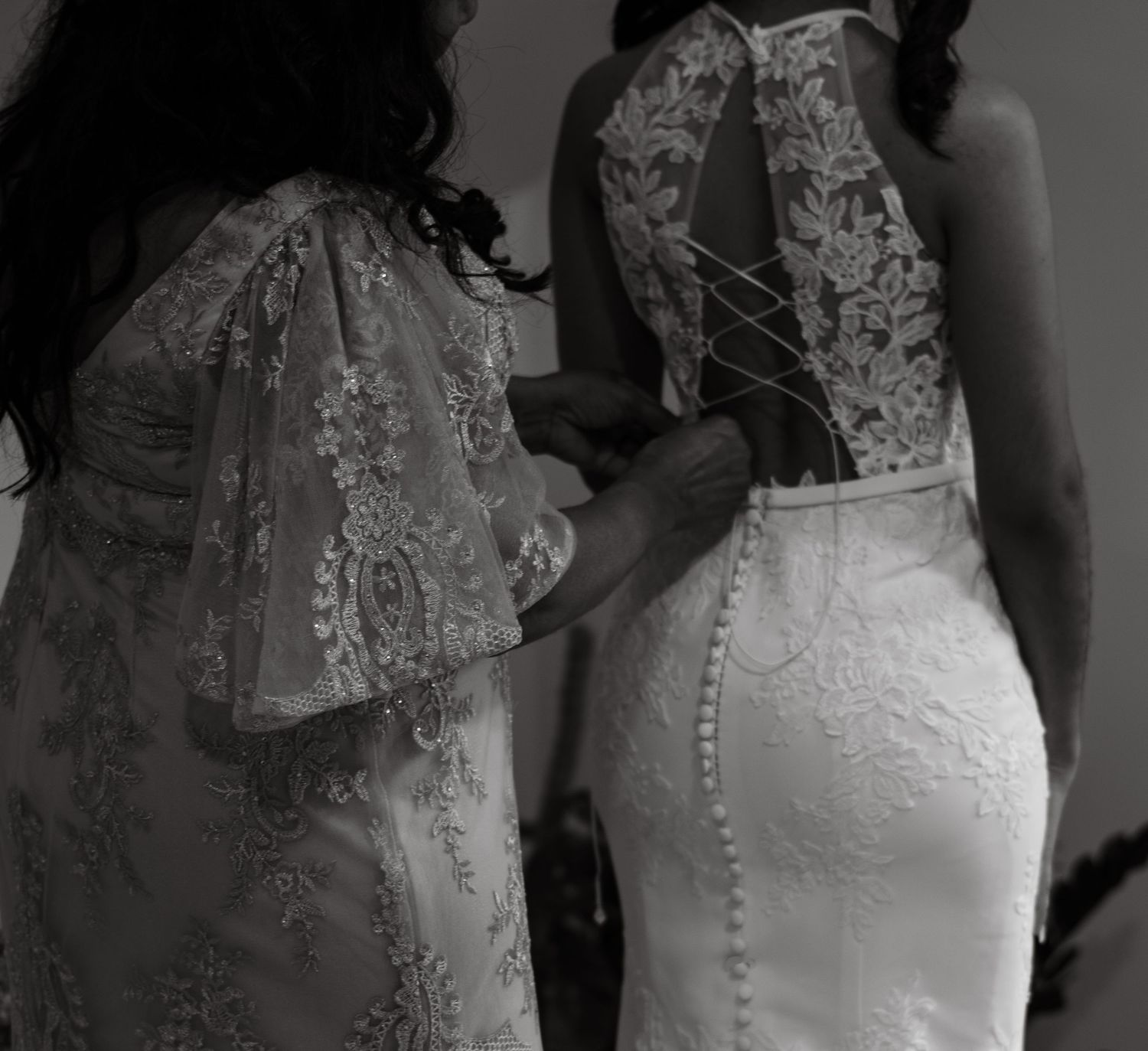 Black and white photo of bridesmaid lacing up the intricate corset back of a lace wedding gown.