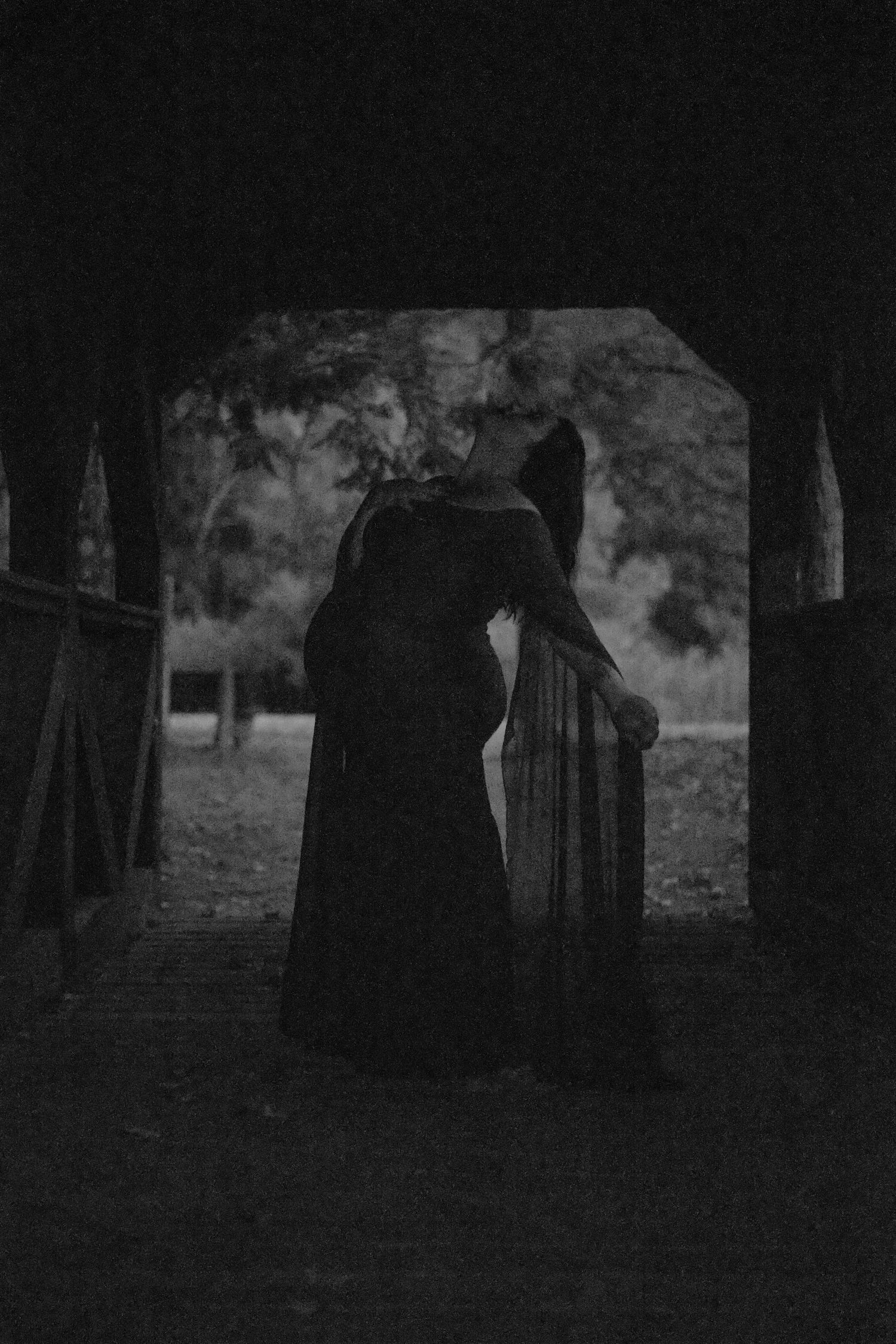 Mysterious dark silhouette of pregnant woman in gown standing in shadowy covered bridge.