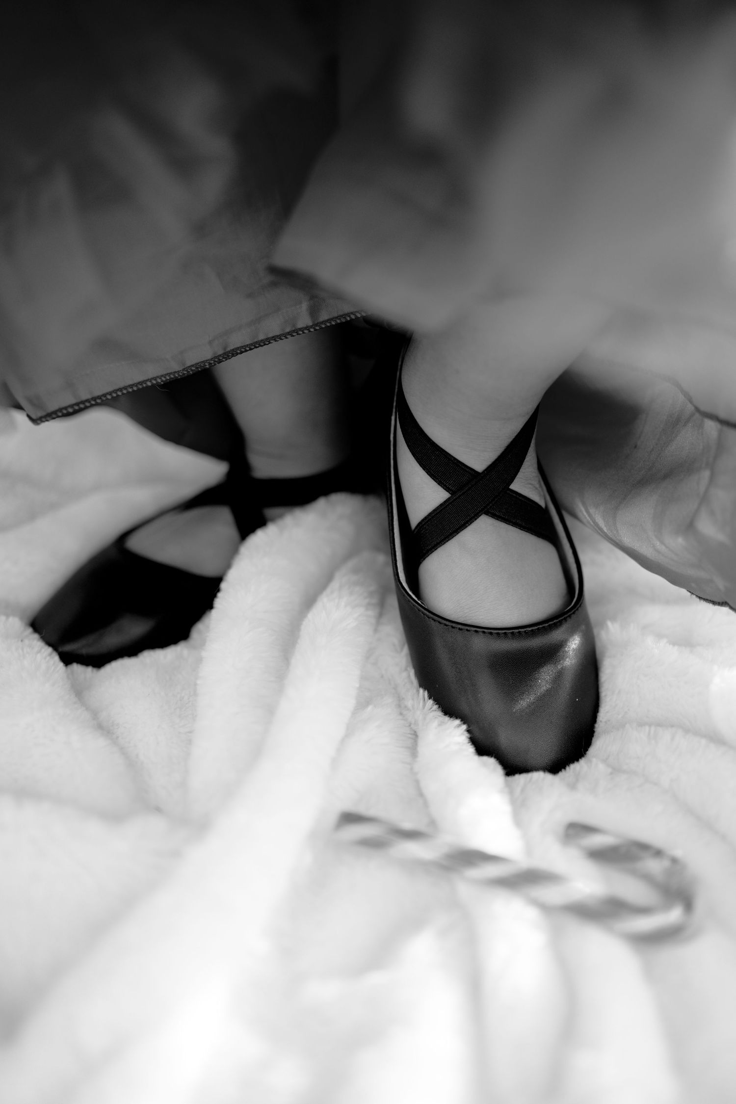 Black and white close-up of a childs feet wearing black ballet slippers surrounded by soft white fabric.