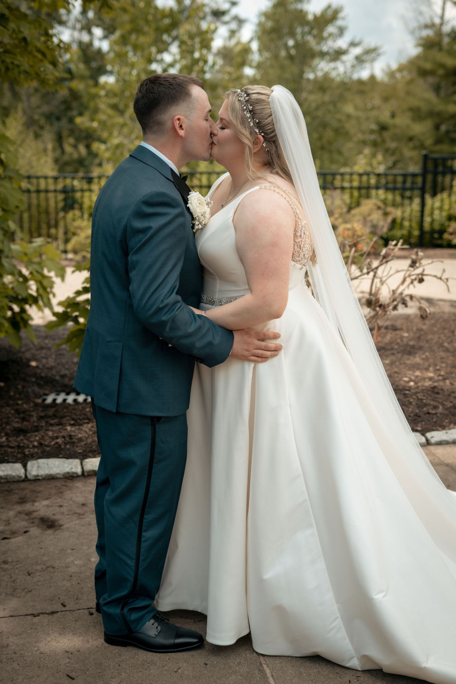 Bride and groom sharing a romantic kiss in a lush garden setting on their wedding day.