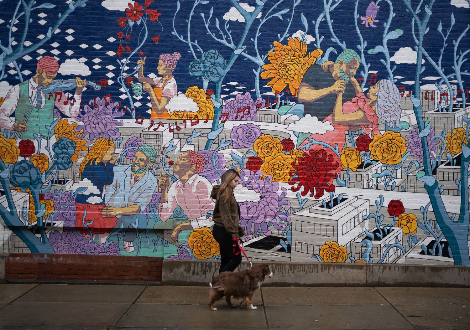 Person walking a dog past a vibrant colorful urban mural featuring flowers and figures on a city sidewalk.