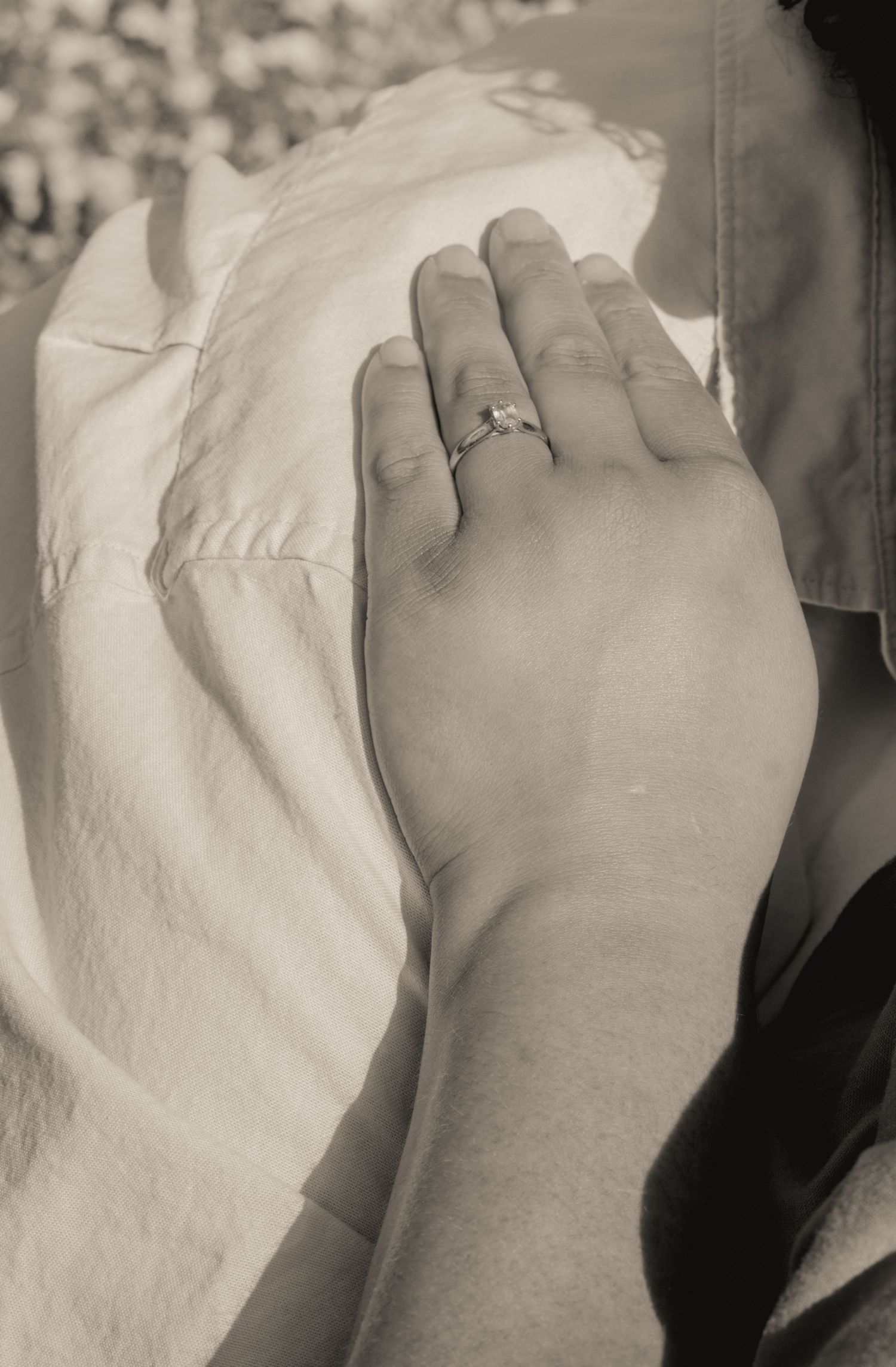 Close-up of woman's hand with diamond engagement ring resting on partner's lap, sepia tone.