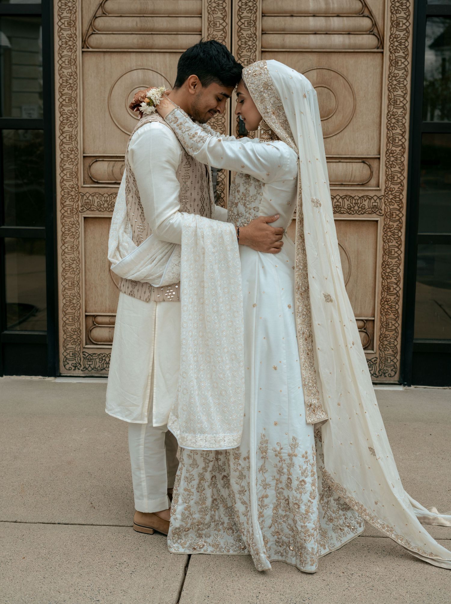 South Asian couple in matching white and gold traditional wedding attire embracing.