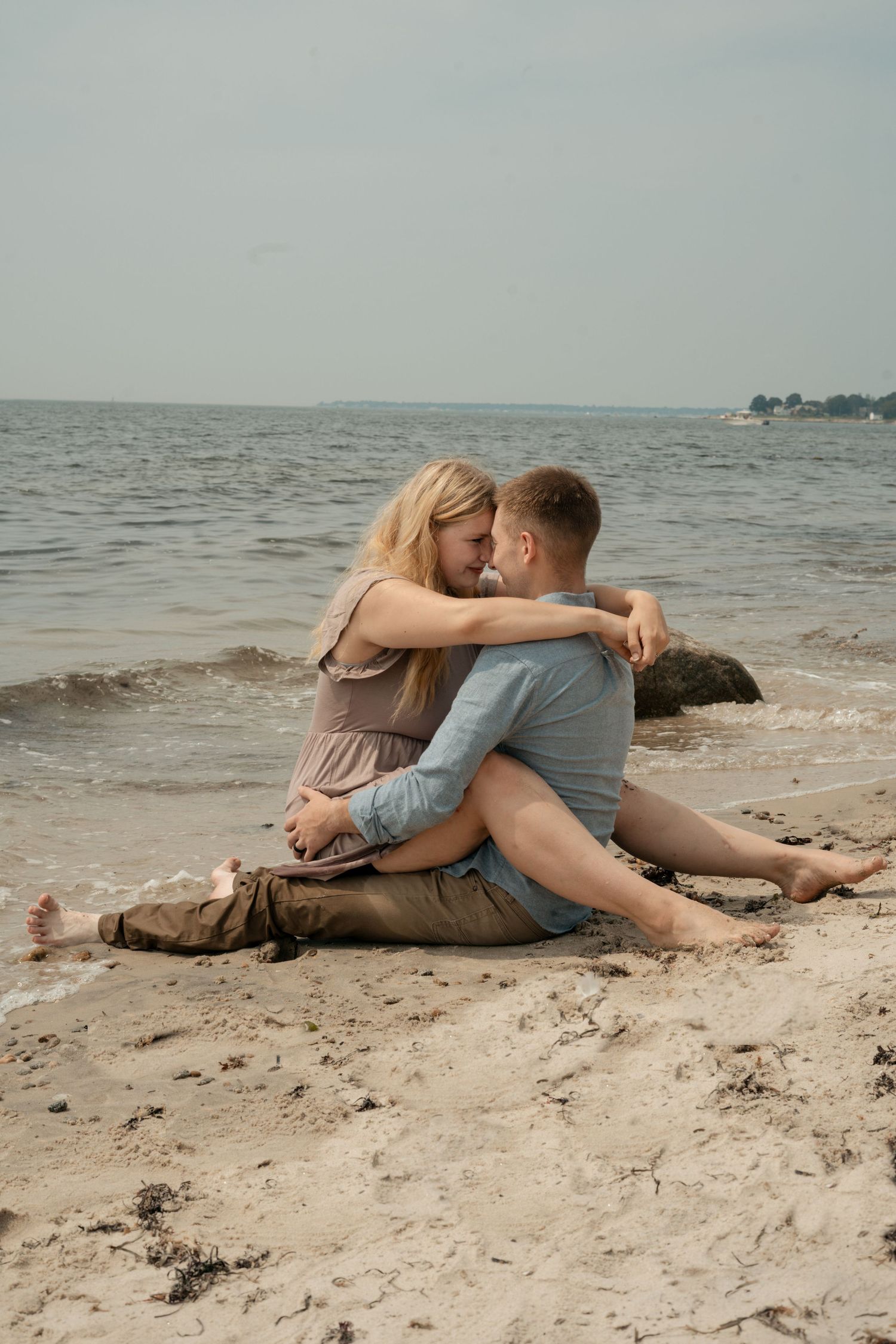 Couple embracing and sharing a tender moment while sitting on a sandy beach by the ocean.