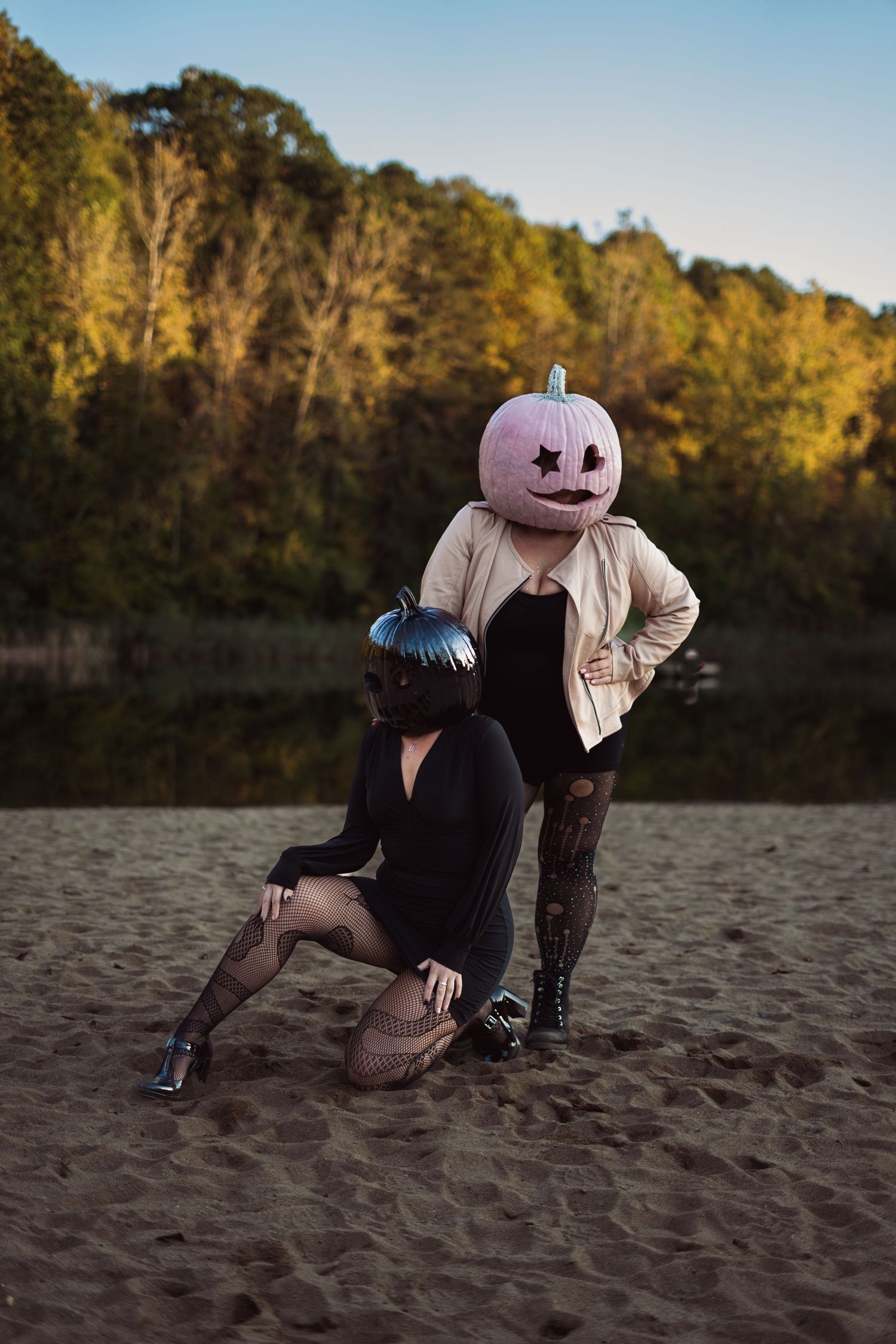 Two people wearing Halloween pumpkin head masks posing on sandy beach at dusk.