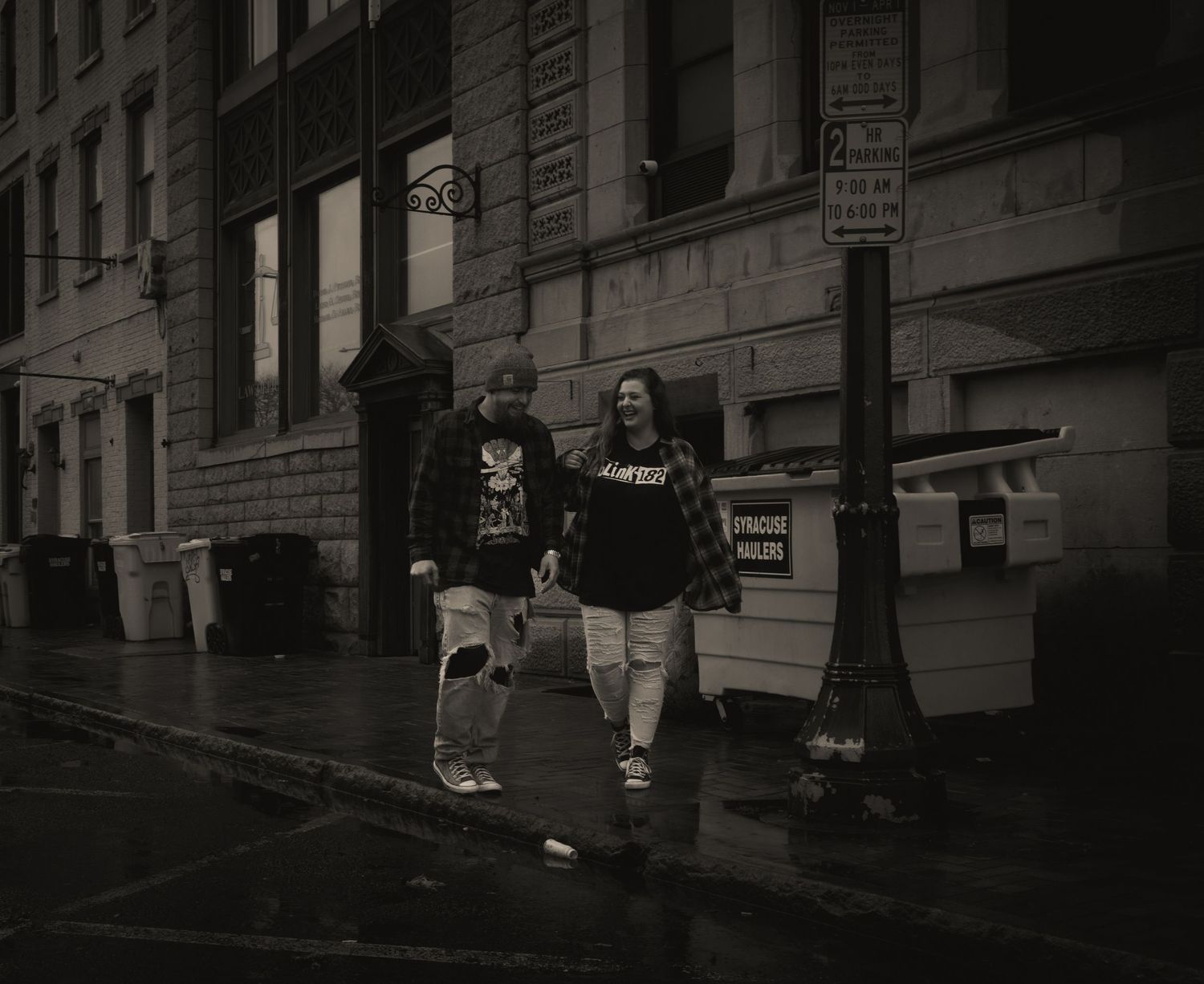 Couple walking hand in hand on wet city sidewalk in black and white.