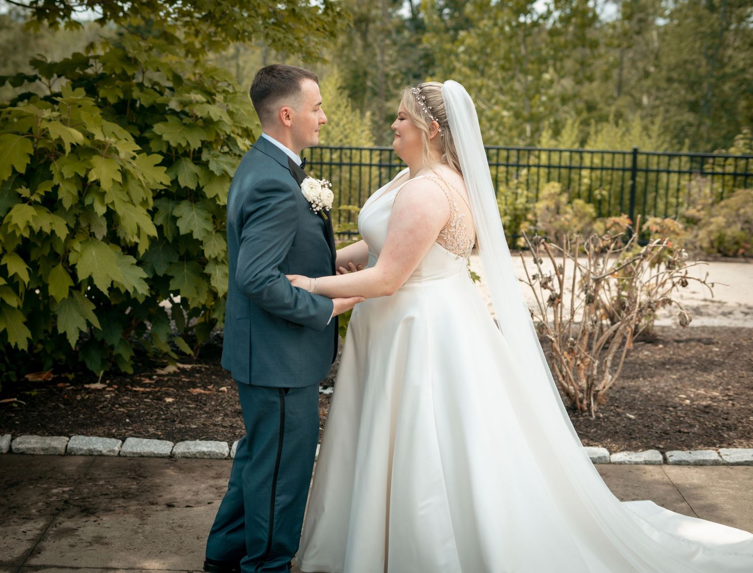 Bride and groom in navy suit sharing a tender first look moment in an outdoor garden setting.