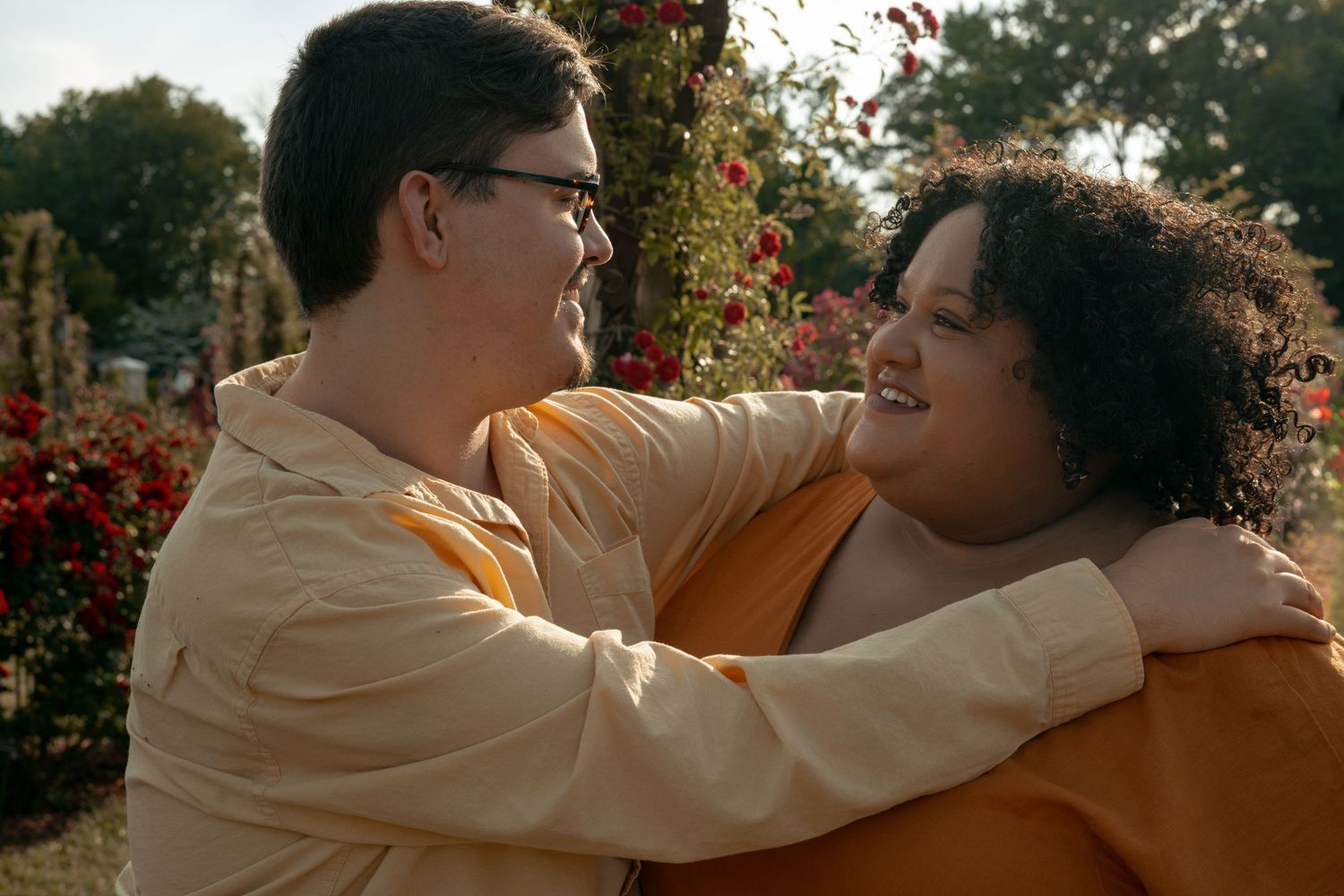 Two people embracing and smiling in a garden with colorful roses blooming in the background.