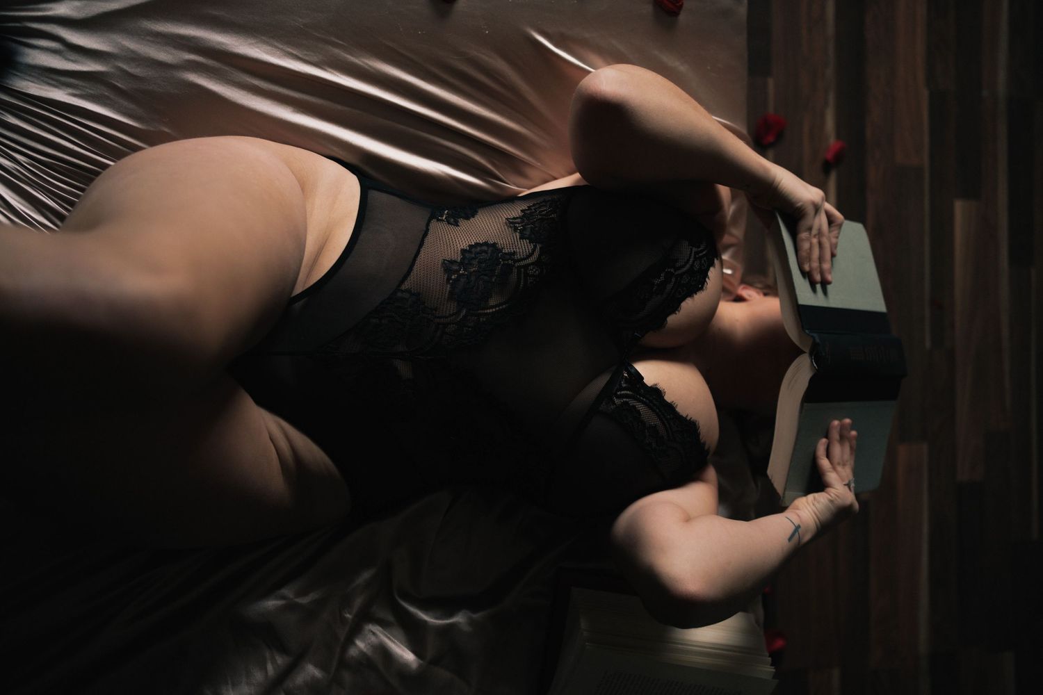 Woman in black lace lingerie poses on bed in dramatic low-key boudoir photography.