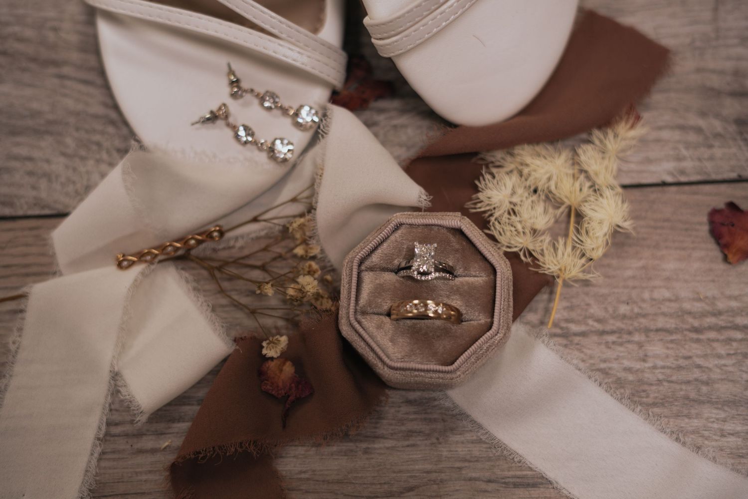 Elegant wedding flat lay featuring diamond ring in velvet box with bridal heels and florals.