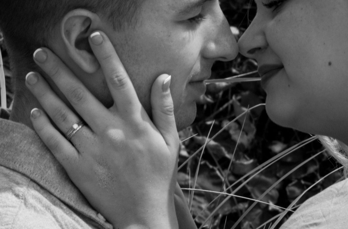 Close-up black and white photo of a couple nearly kissing, with an engagement ring visible.