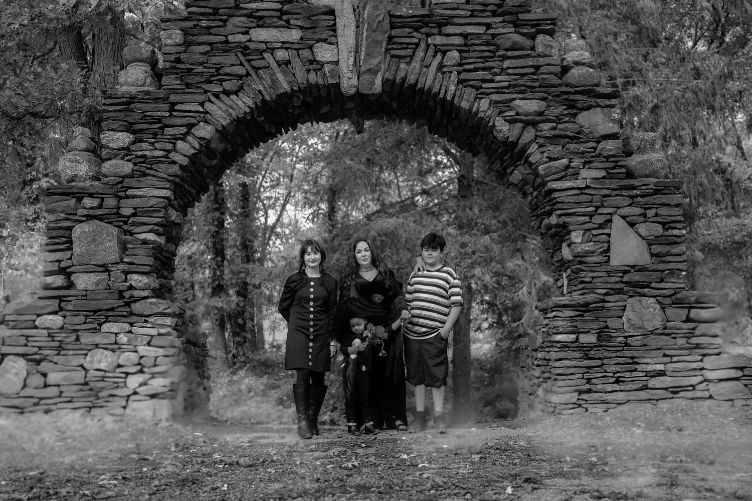 Family in Addams Family costumes posing in black and white under stone arch ruins.