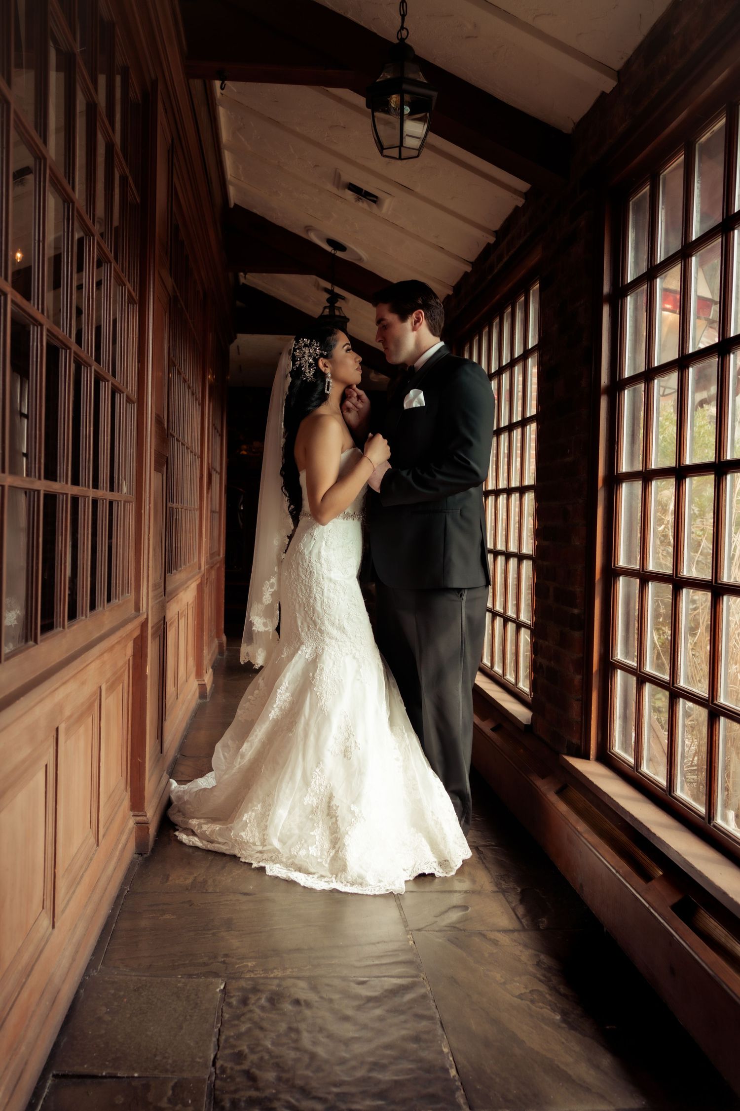Bride and groom sharing an intimate moment in a warmly lit wooden corridor on their wedding day.