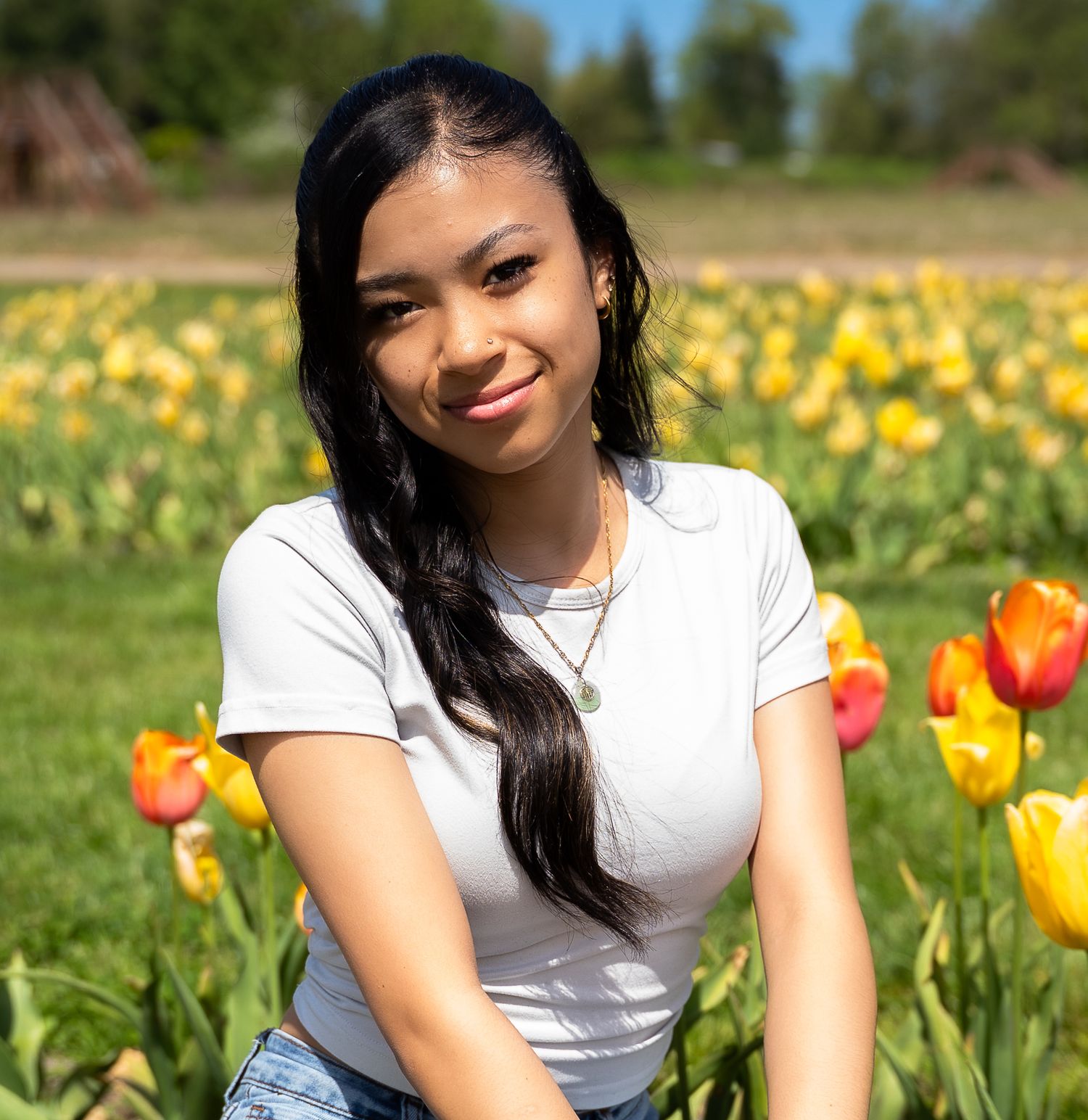 Young woman in white t-shirt sitting among yellow and orange tulips in a sunny field.