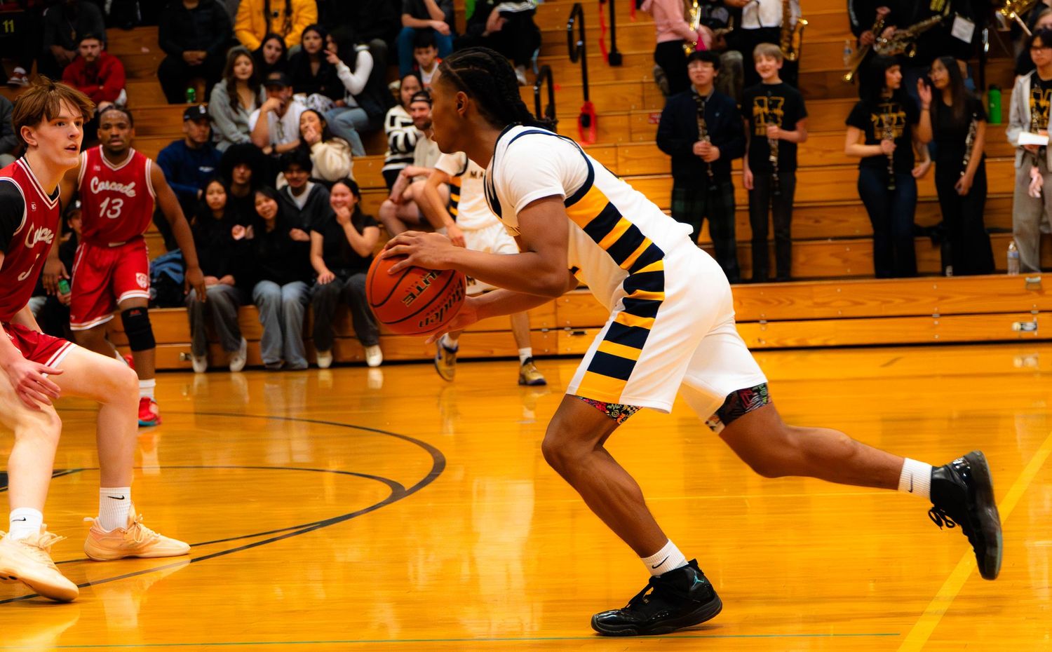 High school basketball player in white and gold uniform dribbles ball during game.