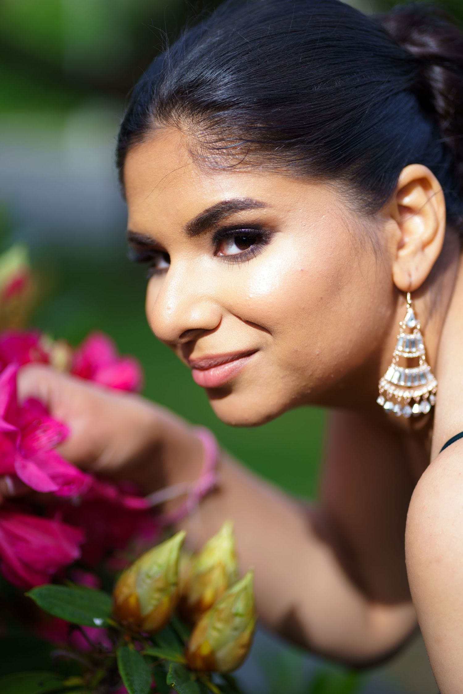 Close-up portrait of woman with elegant chandelier earrings smelling pink roses outdoors.