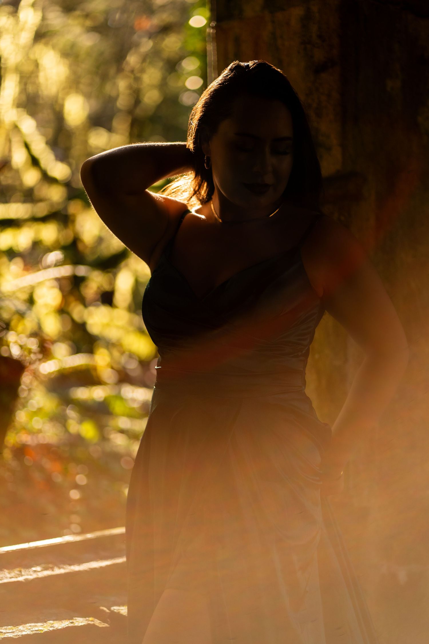 Silhouette of a woman in golden backlight with sun flare in a lush outdoor setting.