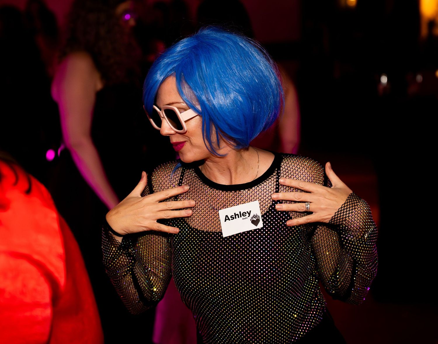 A person with bright blue hair dancing at a nightclub with red and orange lighting effects in the background.