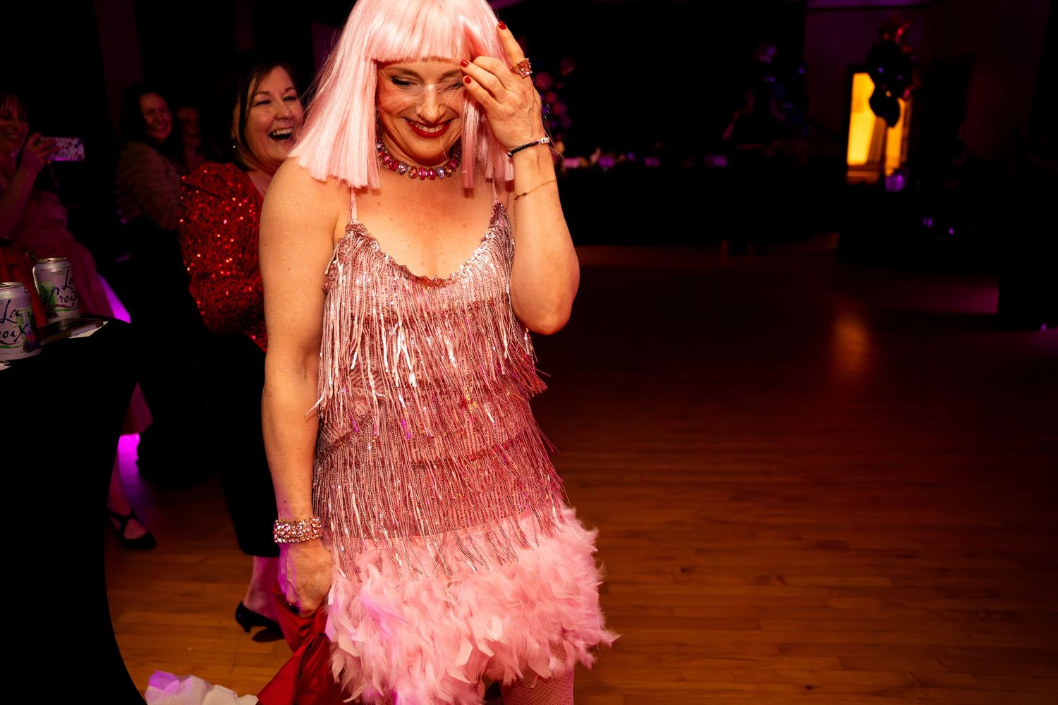 A performer in a pink sequined flapper dress and white wig dances at a festive party event.