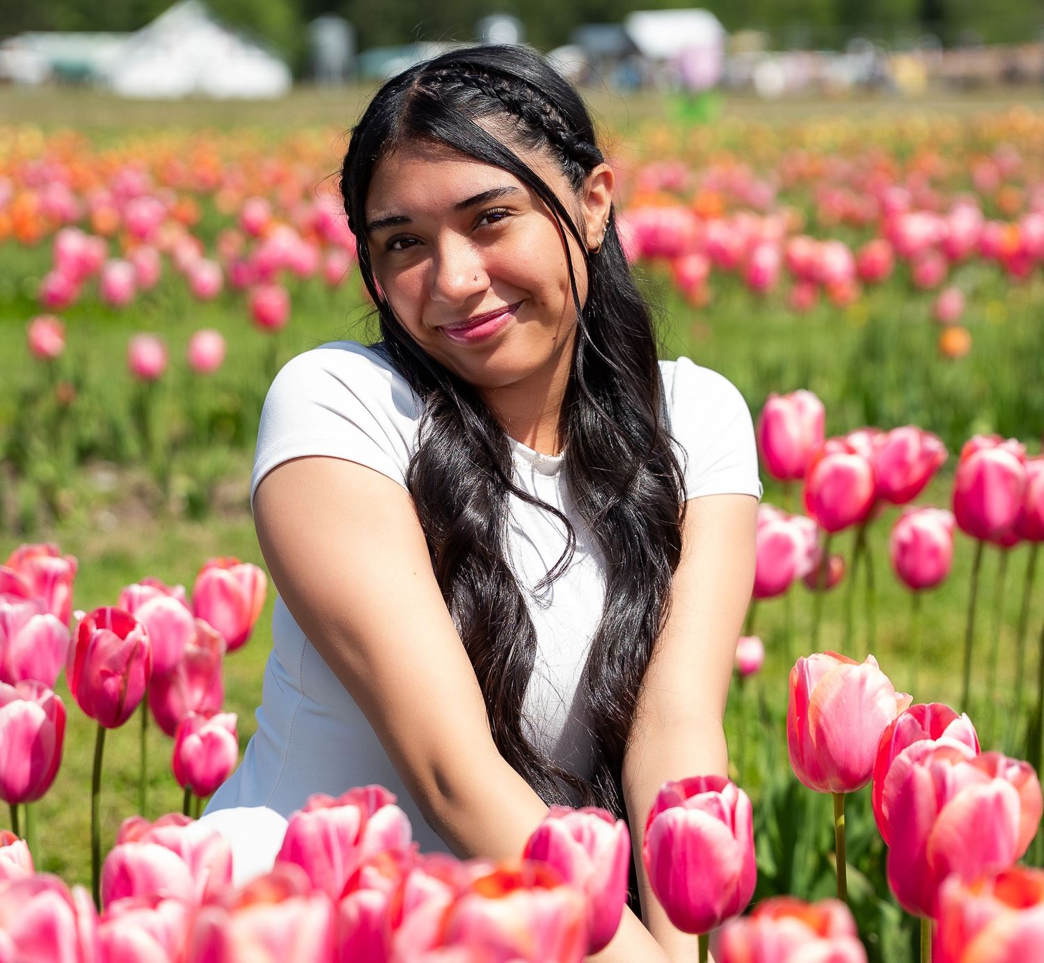 Young woman smiling while sitting among rows of pink tulips in a blooming flower field.