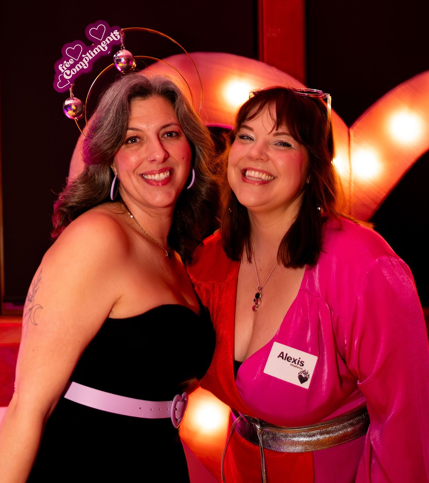 Two smiling women pose together at Valentine's Day party, one wearing bachelorette tiara.