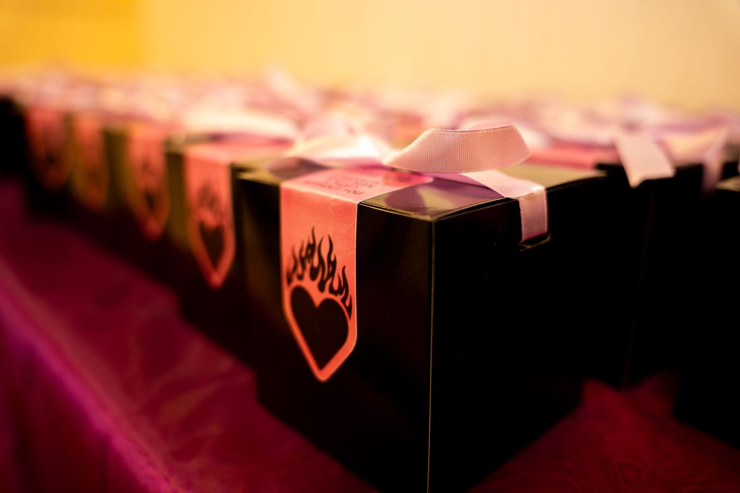 Row of black gift boxes with flaming heart design and pink ribbon bows at event.