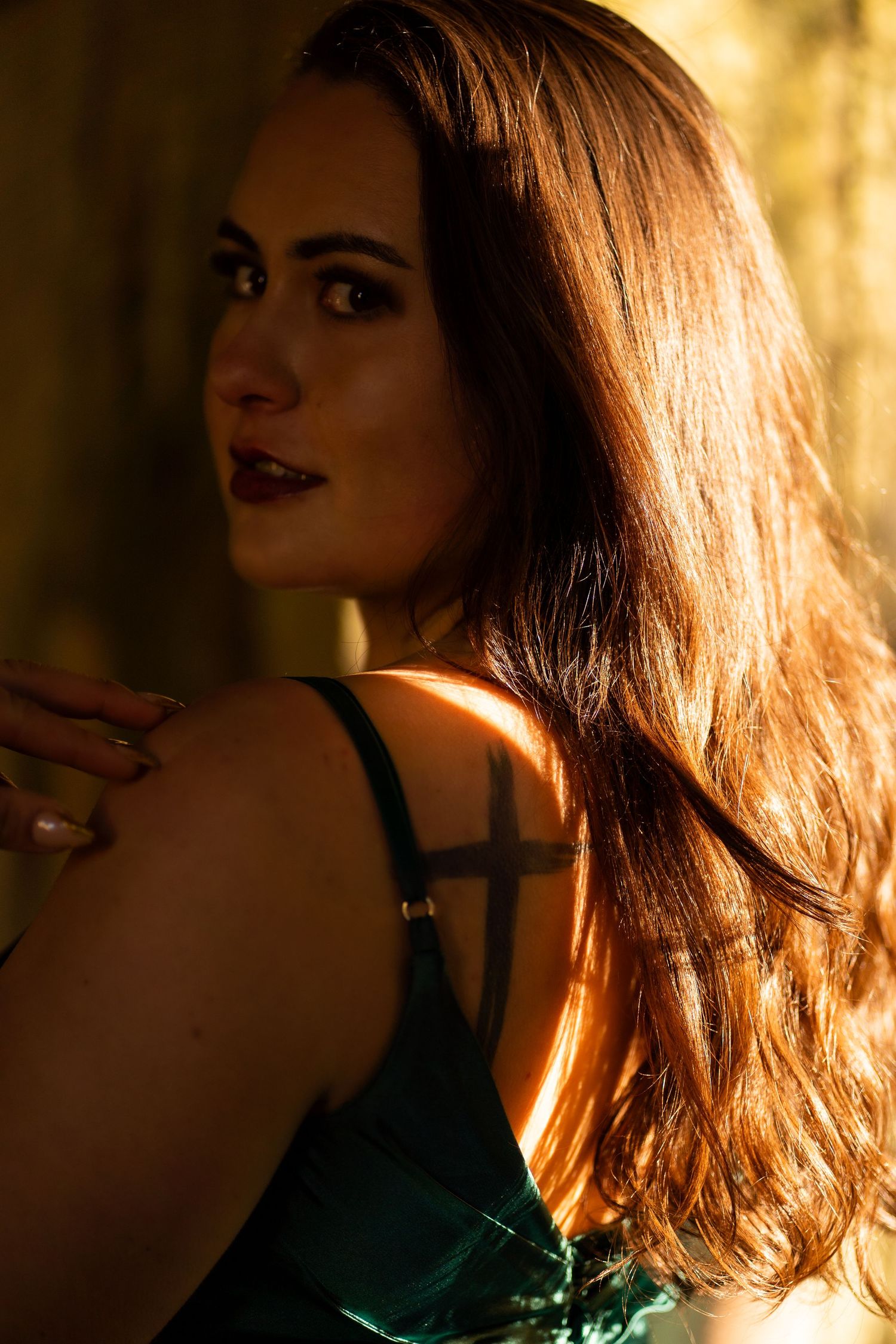 Woman in green dress with warm golden backlight highlighting long brown hair.