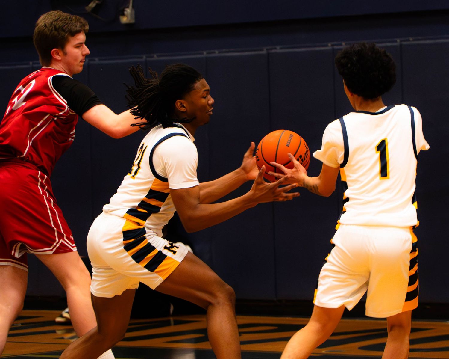 Two Mariner basketball players work together to secure the ball against a red-uniformed opponent.