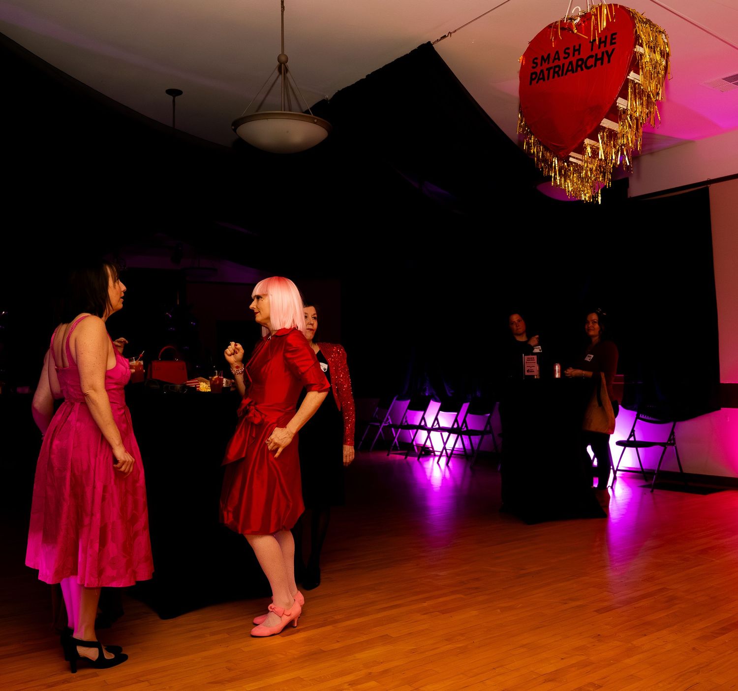 Guests dance under decorative heart pinata at dimly lit Valentine's Day party venue.