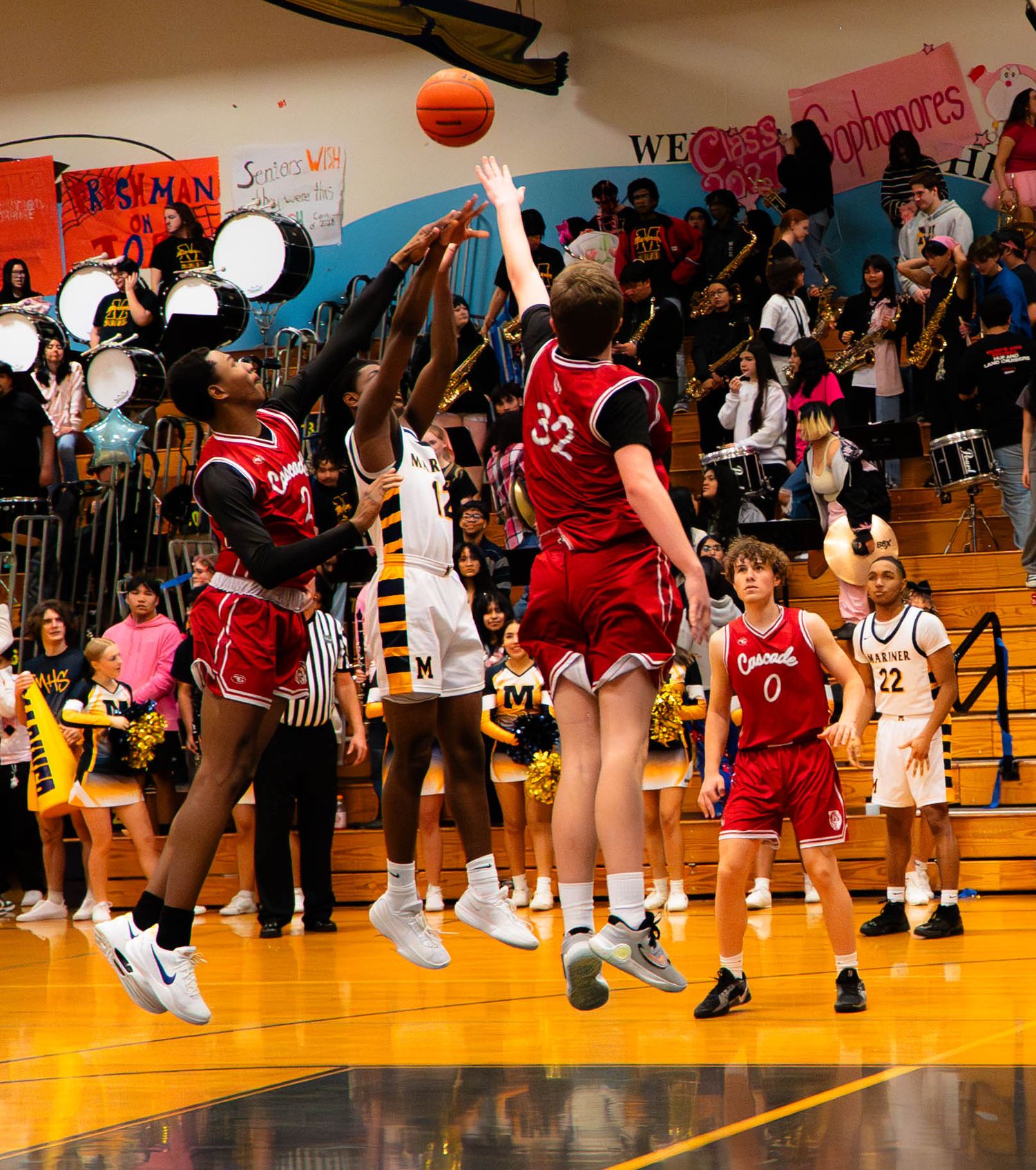 Basketball players jump for the ball during an intense high school gymnasium game.