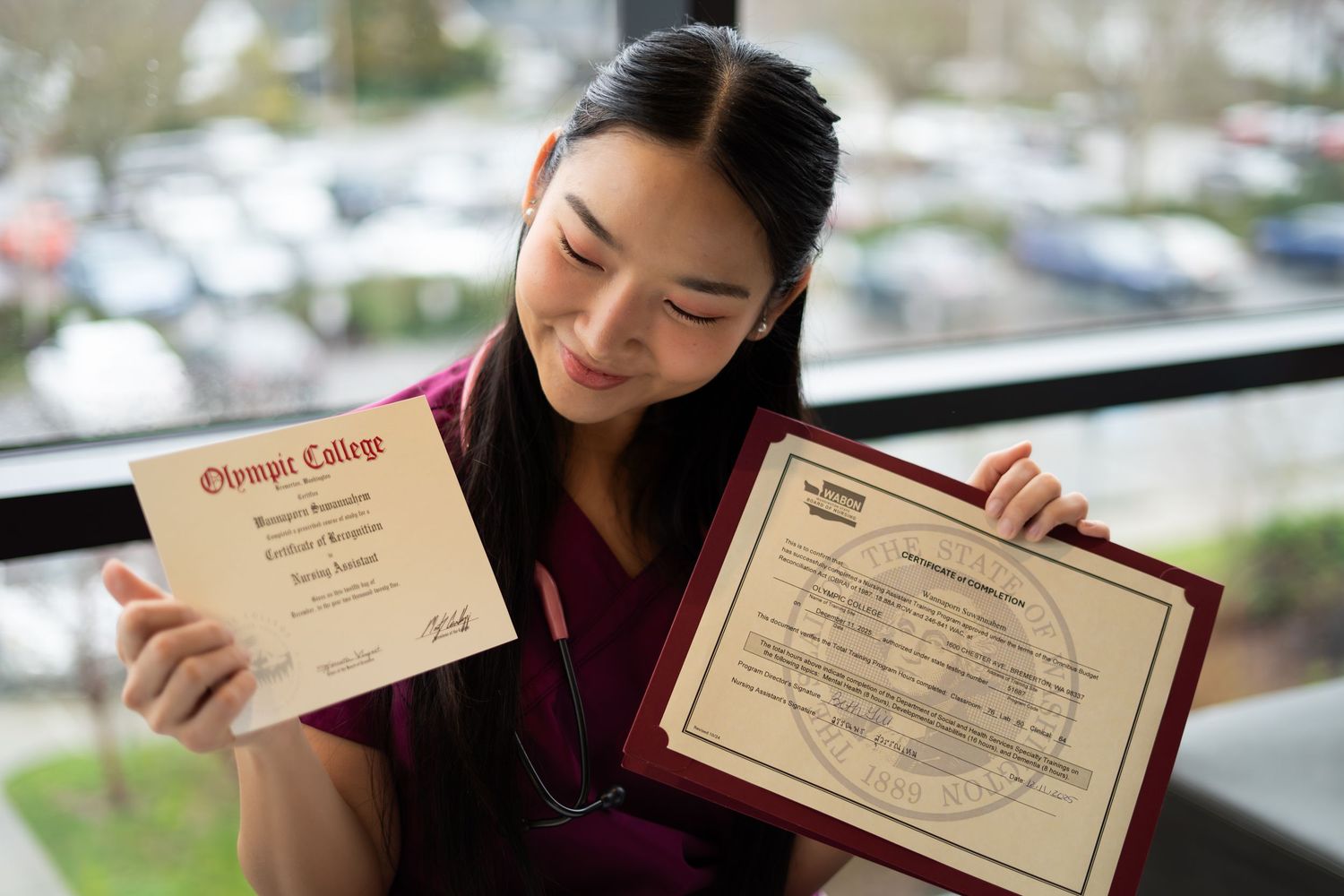 Young woman in nursing scrubs proudly displaying Olympic College nursing diploma.