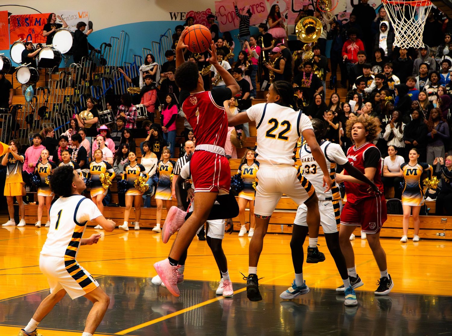 Players battle for a rebound during a high school basketball game in a packed gymnasium.