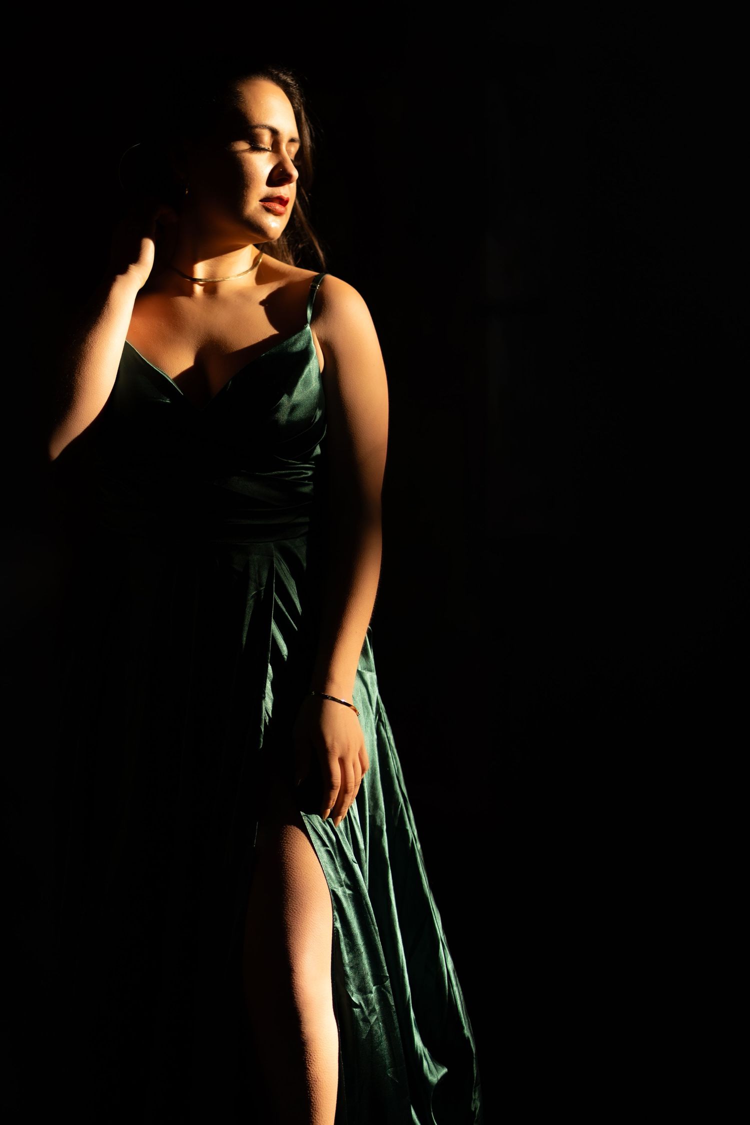 Elegant woman in emerald green evening gown posed dramatically against dark background.