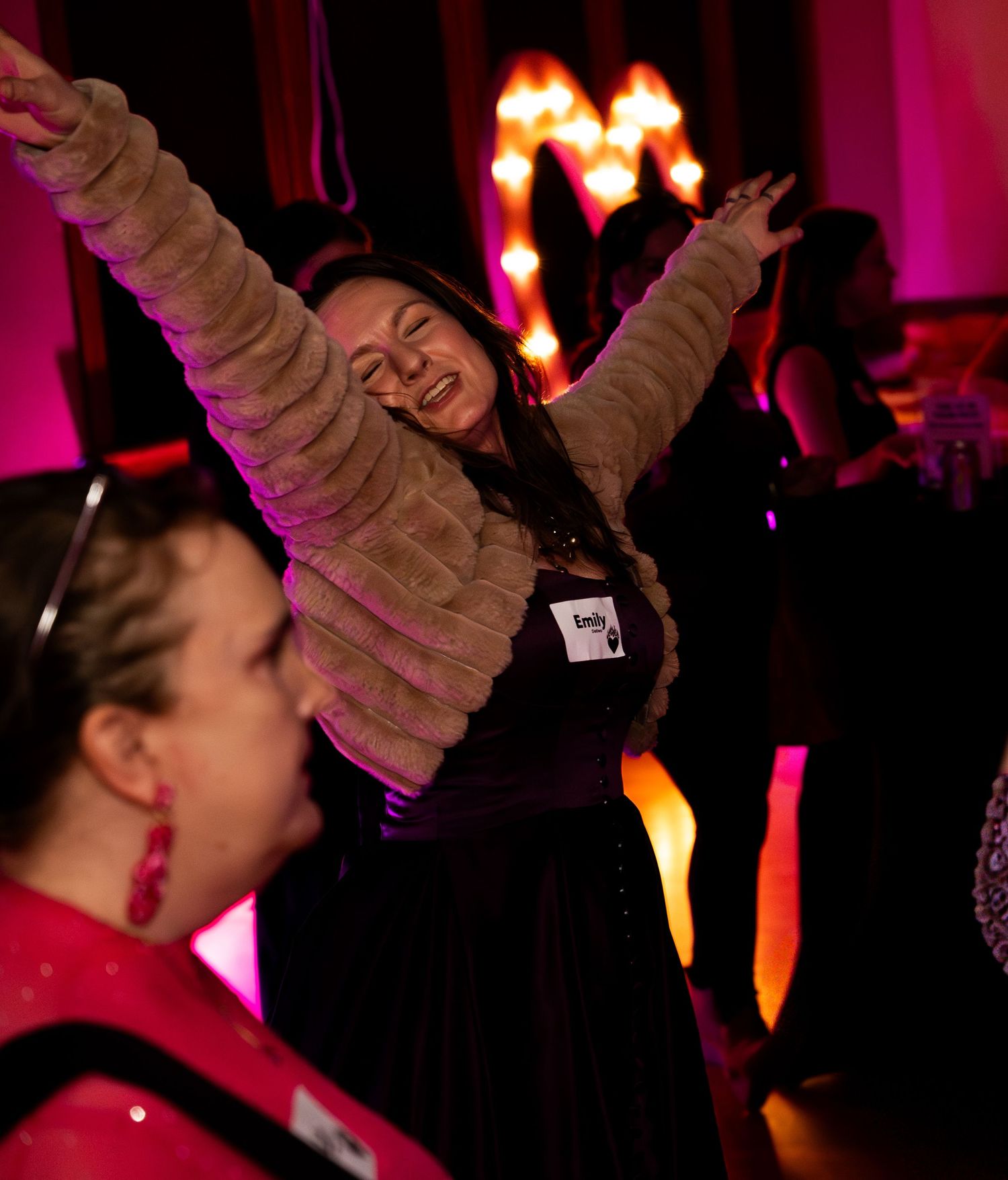 Joyful woman raises arms in celebration on dance floor at festive evening party event.