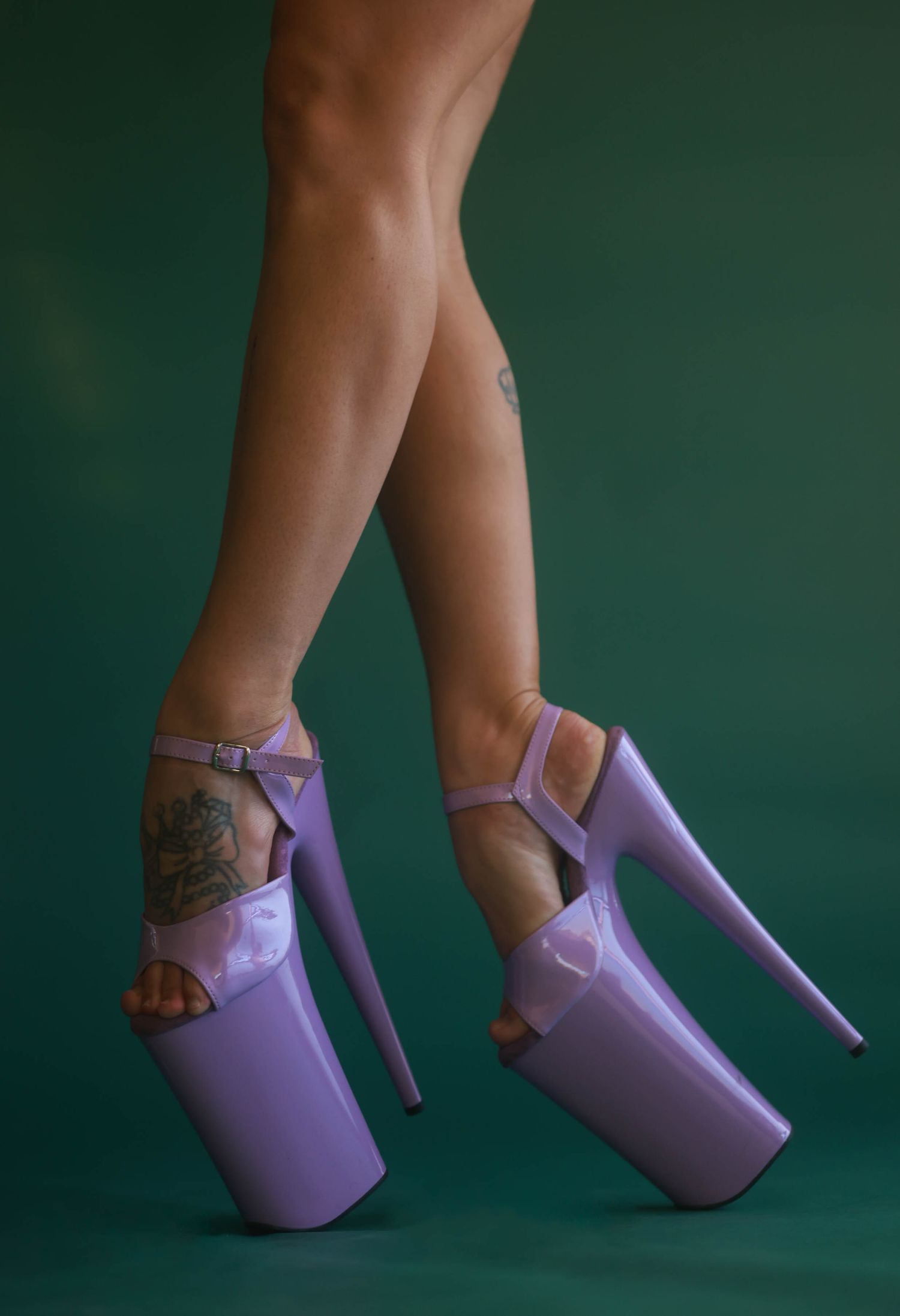 Close-up of legs wearing lavender platform high heels with ankle straps on a green background.