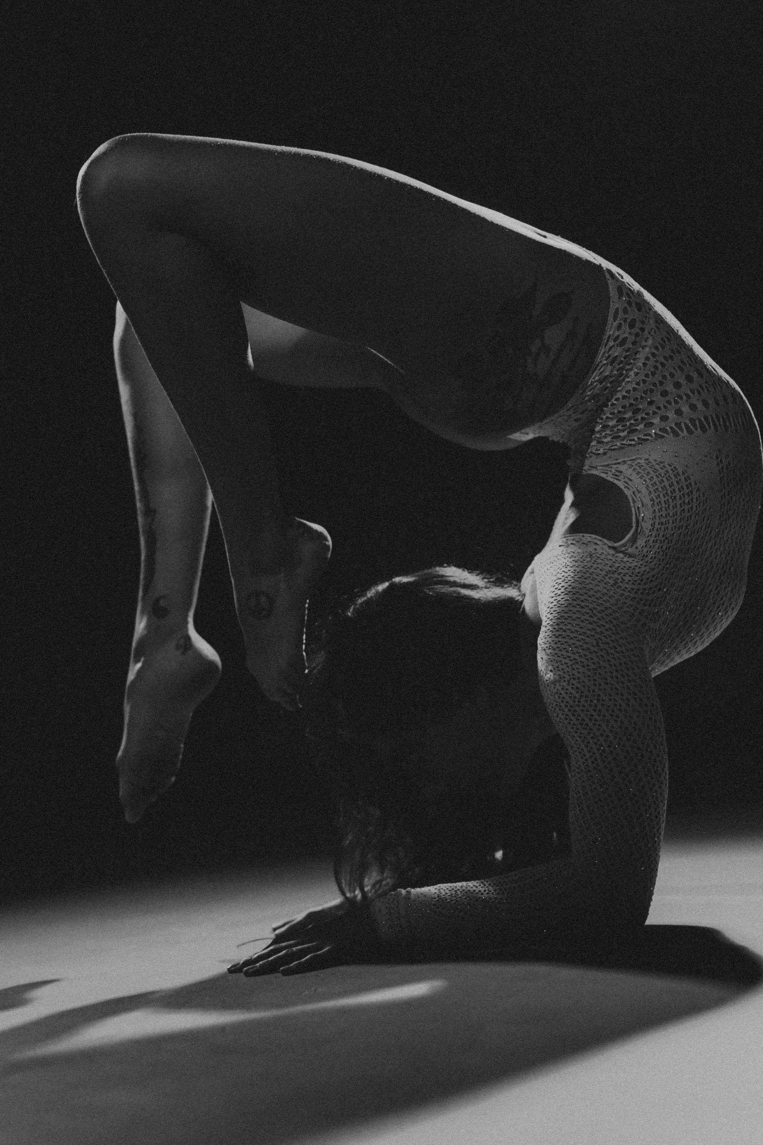 Black and white photo of a flexible dancer in a deep backbend pose on the floor, wearing a patterned leotard.