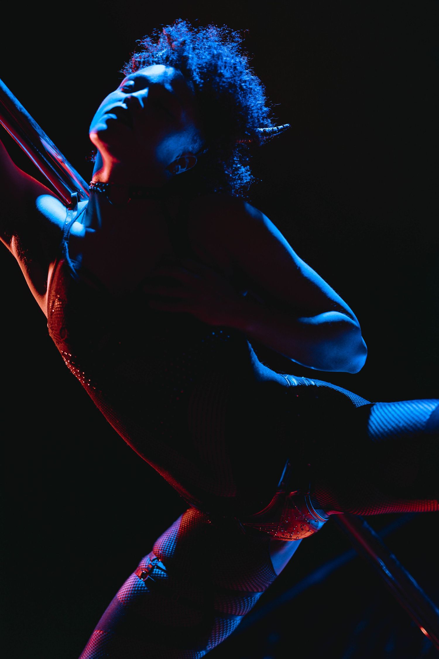 Artistic silhouette of a pole dancer illuminated by blue and red neon lights in darkness.