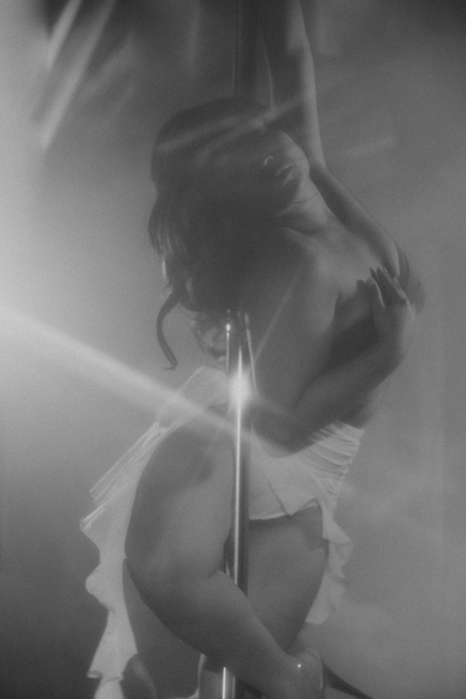 Black and white photo of a woman dancing around a pole under dramatic stage lighting.