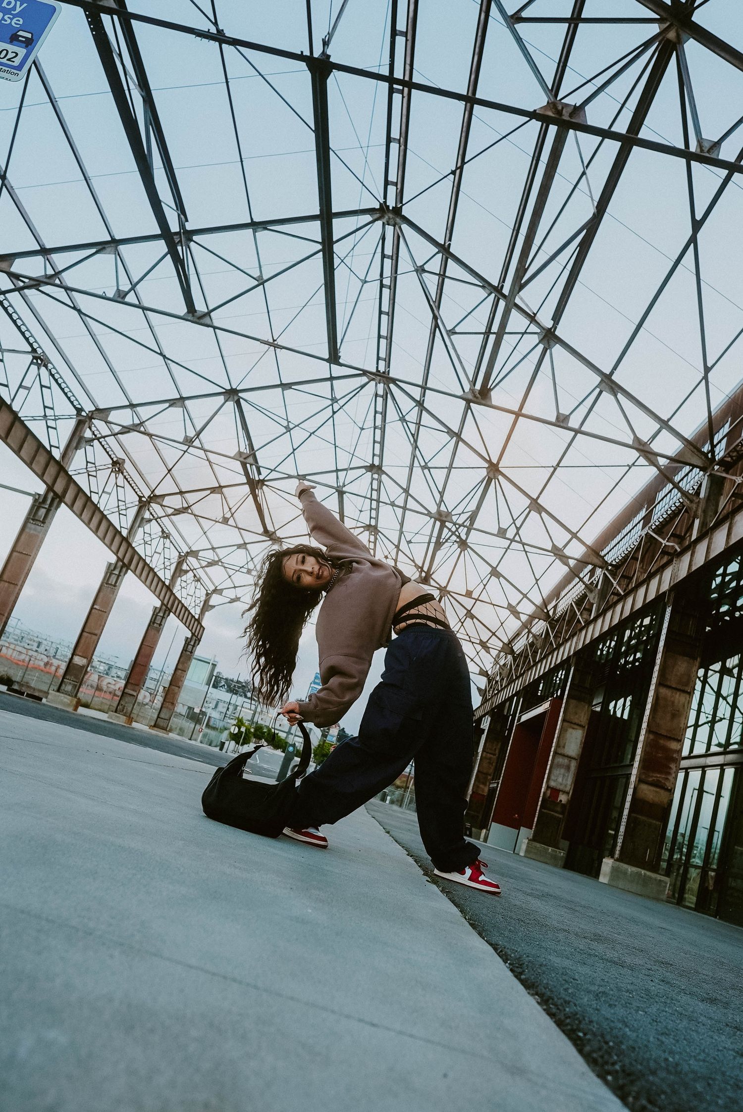 A breakdancer performs a dynamic move under a geometric steel structure in an urban setting.