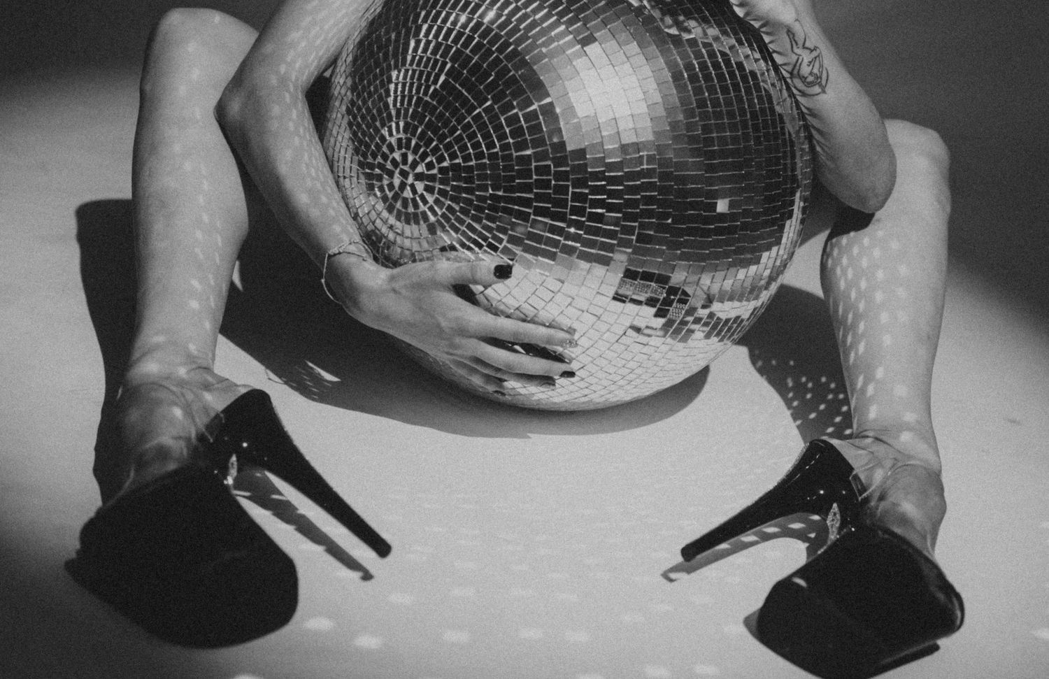 Black and white close-up of hands holding a disco ball with platform heels visible.