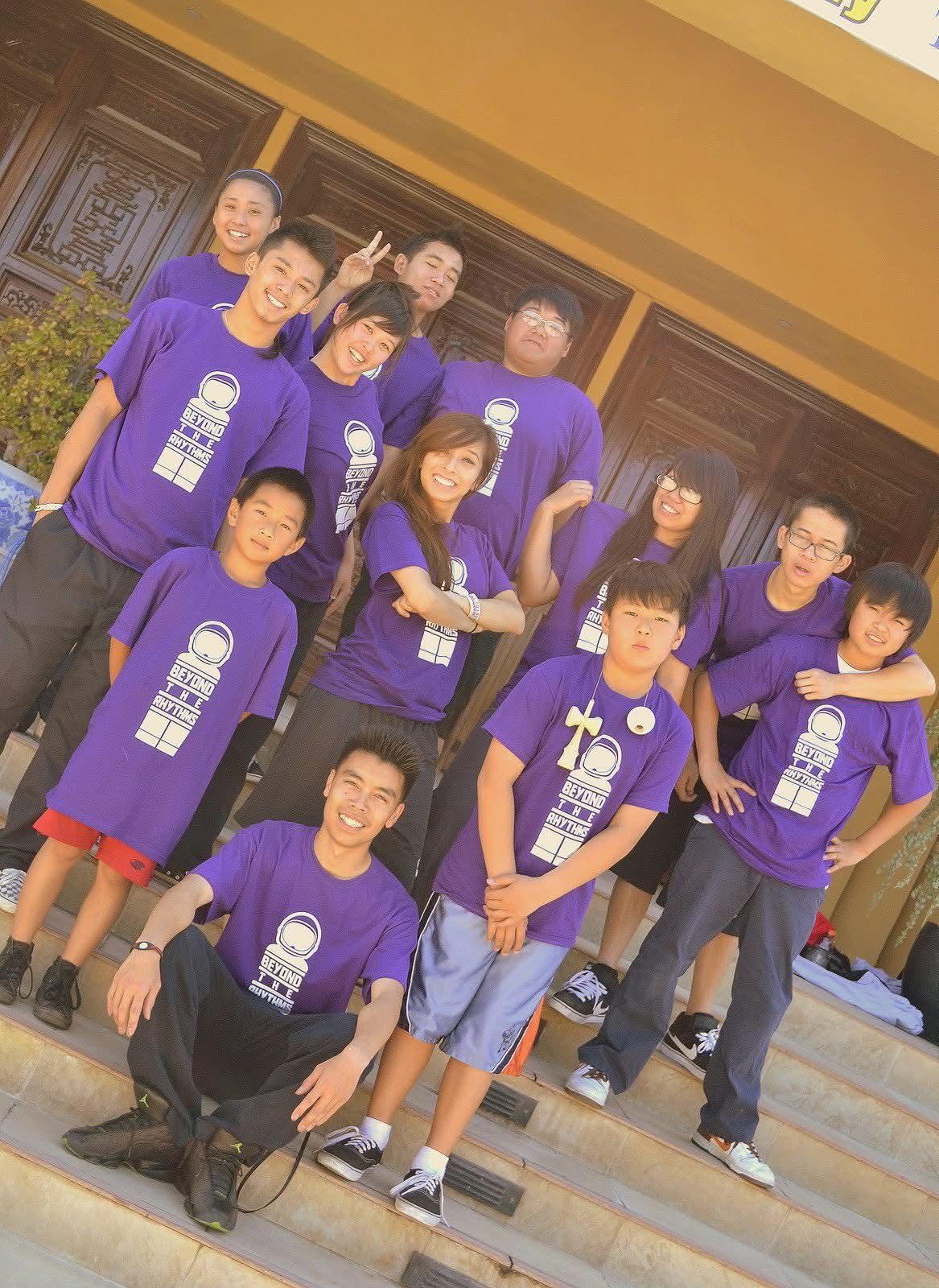Group of young students posing in matching purple t-shirts on steps outside a building.