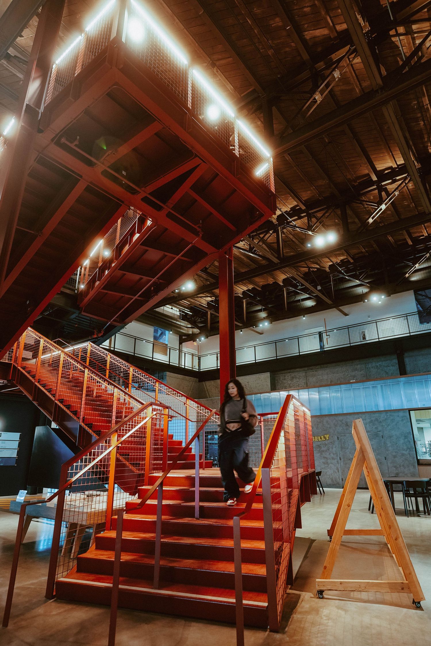 Woman descending bold red industrial staircase in a warmly lit modern warehouse interior.